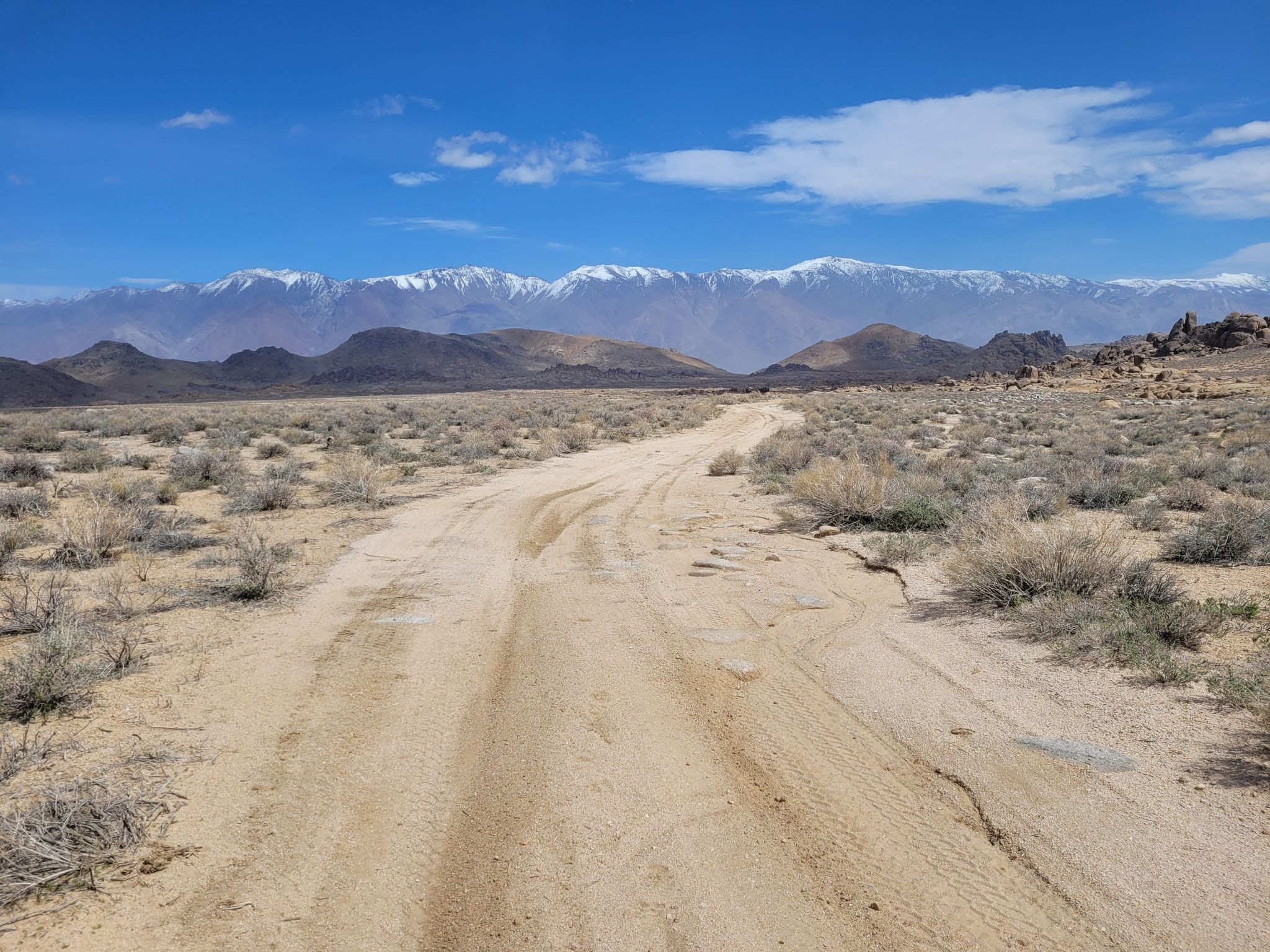 Wide dirt road through arid landscape with distant snow-covered mountain range. - Upper Alabama Hills Trail to Cyclops Skull Arch