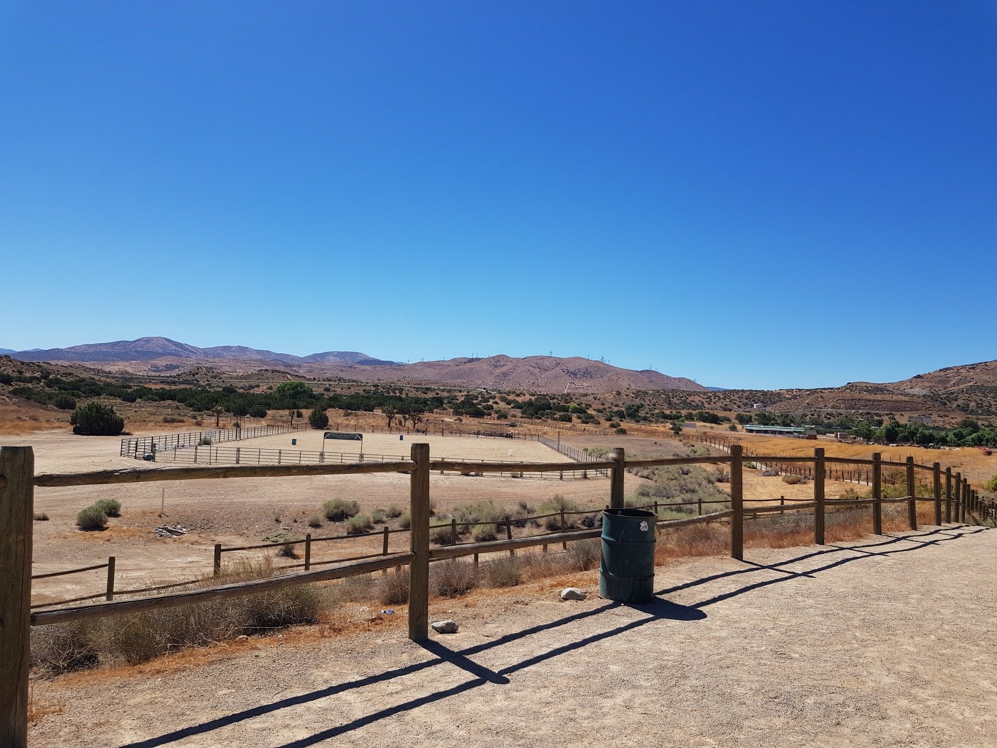 A fenced dirt arena with distant mountains under a clear blue sky. - Barrel Springs Trail