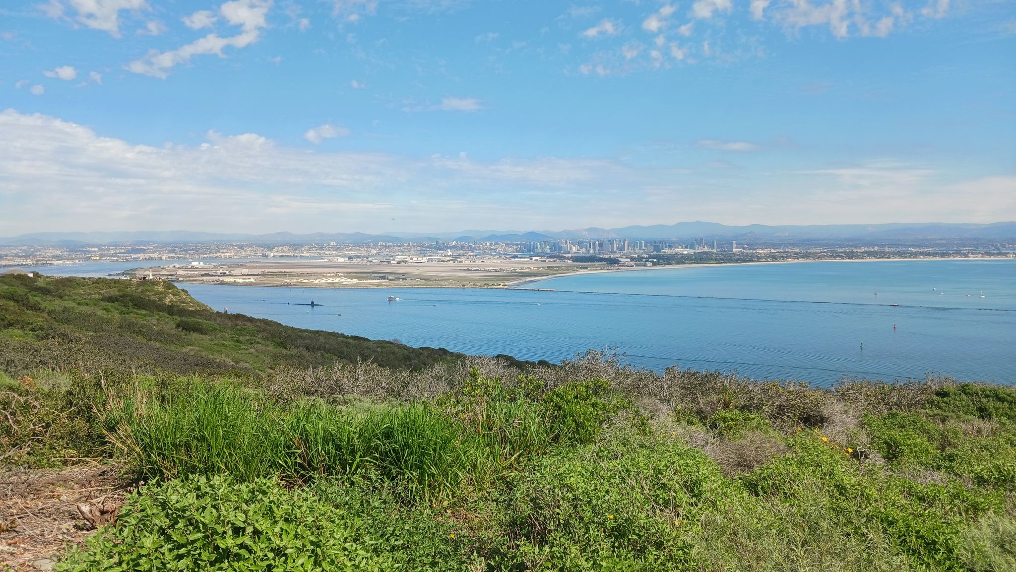 Bright day overlooking a bay, distant city, and green coastal hills. - Old Point Loma Lighthouse loop from Cabrillo National Monument
