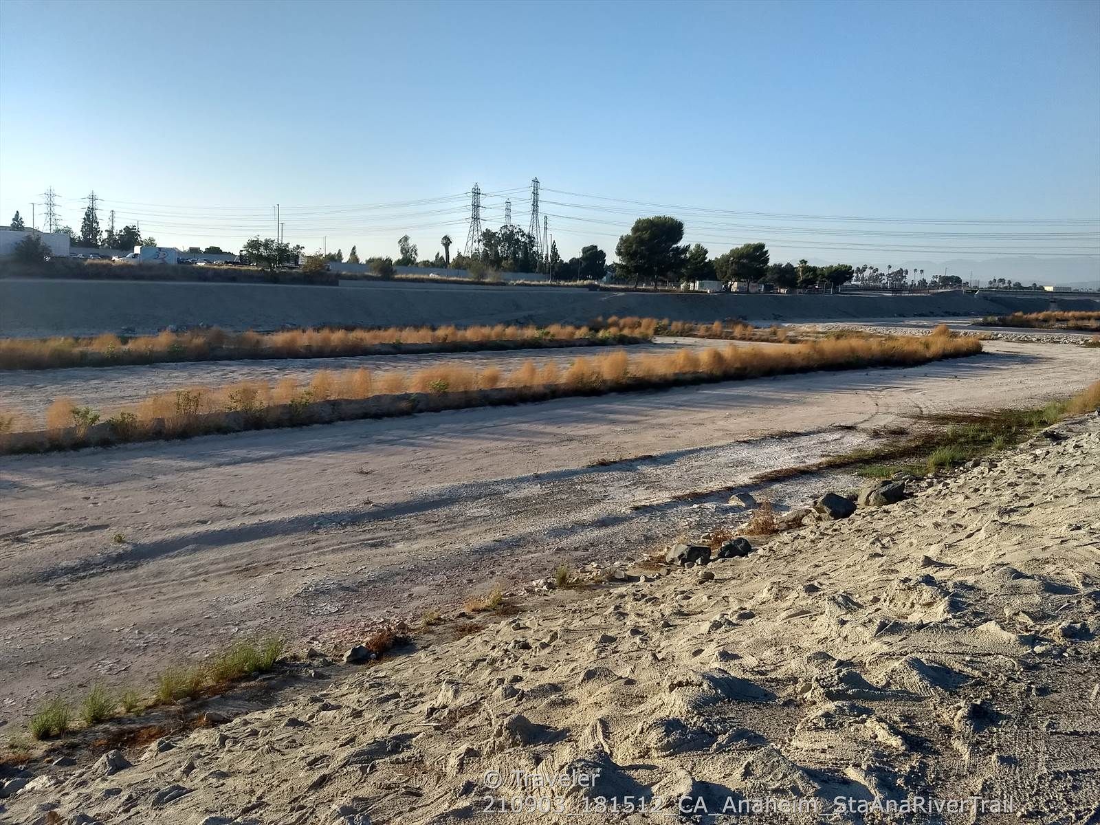 Dry riverbed with sparse brown vegetation, power lines, under clear sky. - Talbert Regional Park – Santa Ana River Trail loop from Huntington Beach International Surfing Museum