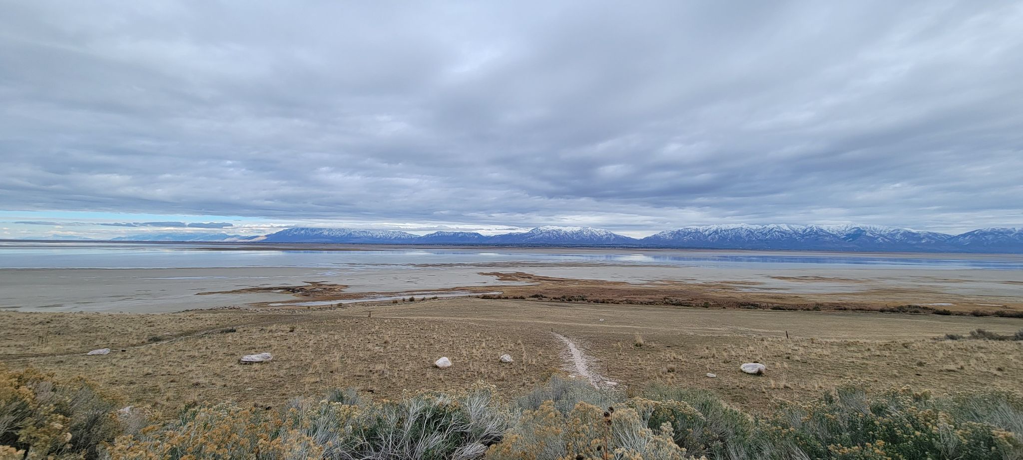 Overcast view of a vast lake, dry land, and distant snow-capped mountains. - Antelope Island to Fielding Garr Ranch Cycle Route