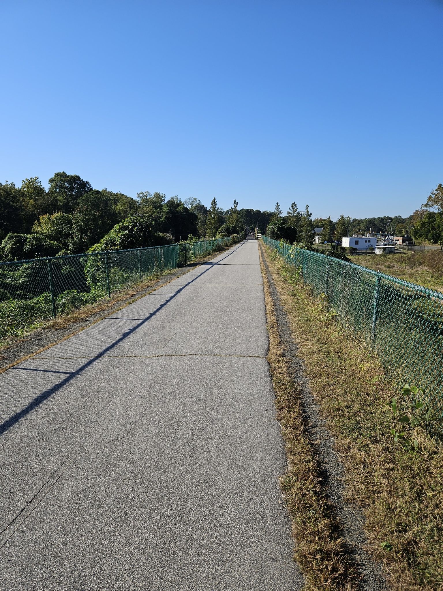 A long paved path stretches under a clear blue sky, fenced. - American Tobacco Trail – American Tobacco Trail loop from Durham