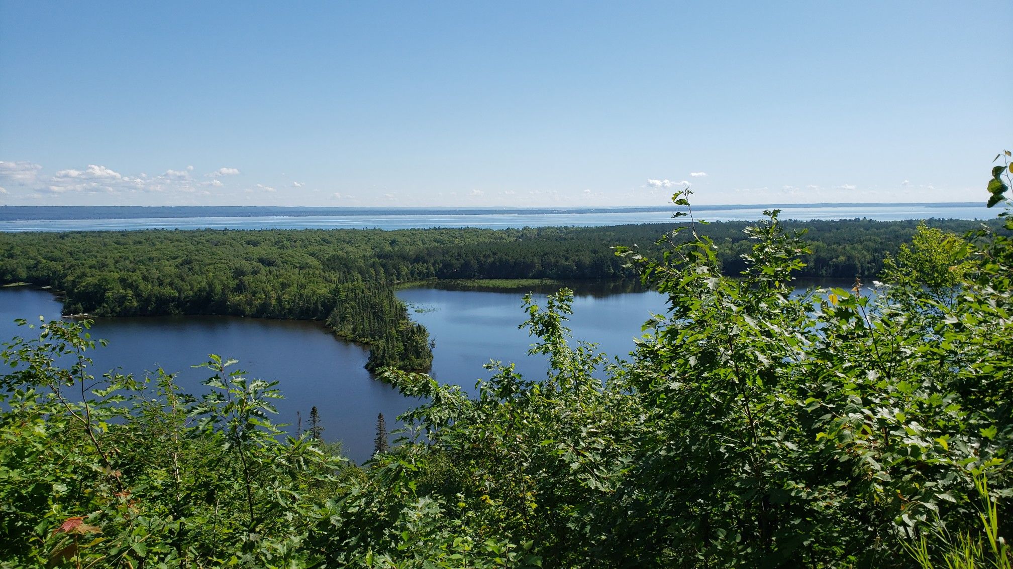 Overlook of a dark blue lake surrounded by dense green forest under a clear sky. - Mission Hill Trail