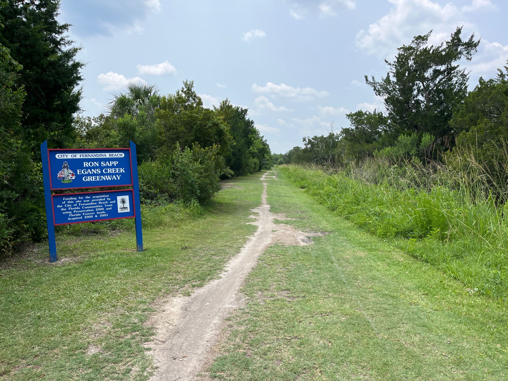 Grassy path next to a blue sign, leading into a green landscape. - Running loop from Amelia Island Light