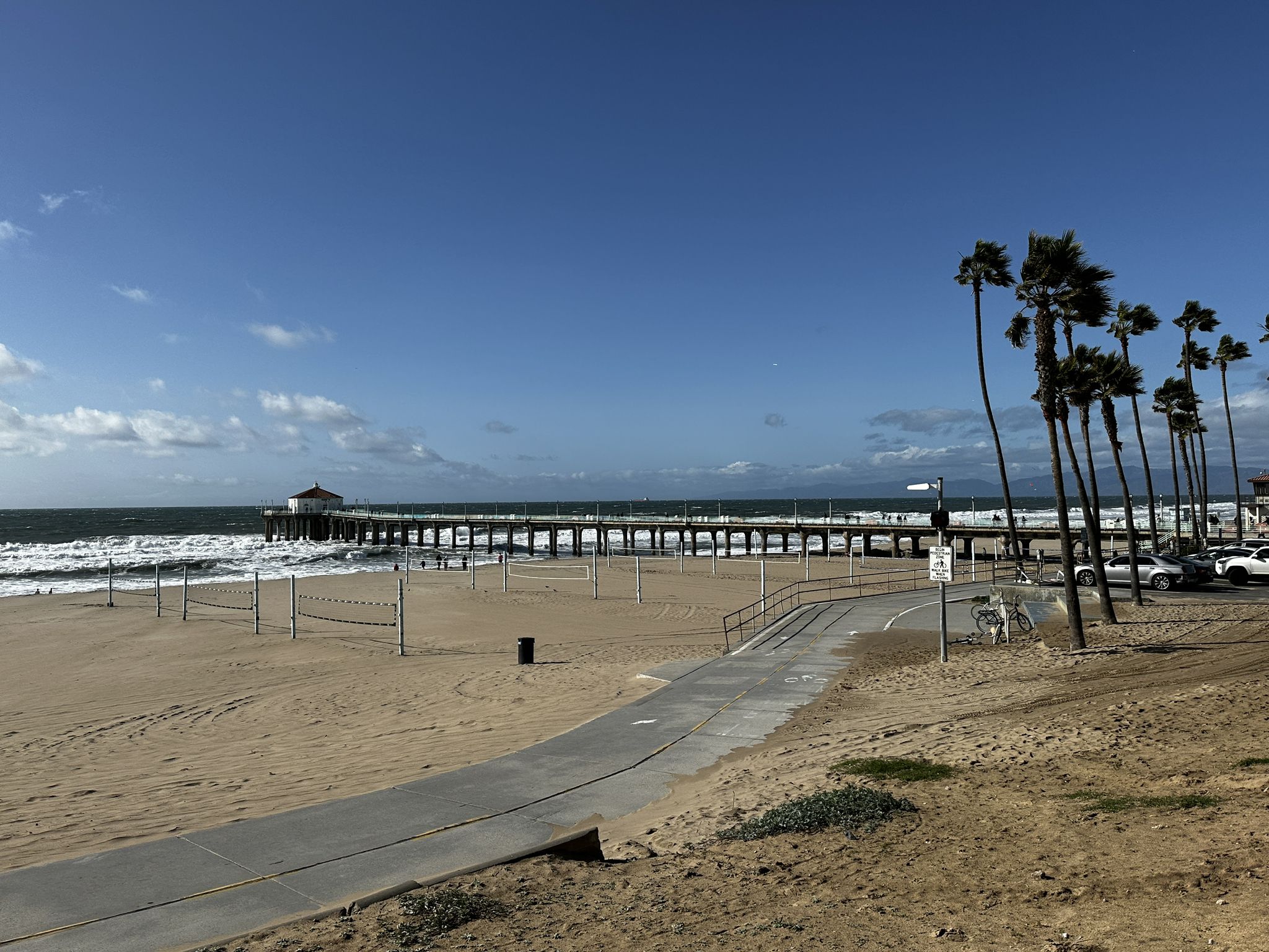 Sunny beach with a pier, volleyball nets, paved path, and palm trees. - Manhattan Beach and Pier – Noble Park loop from Manhattan Beach
