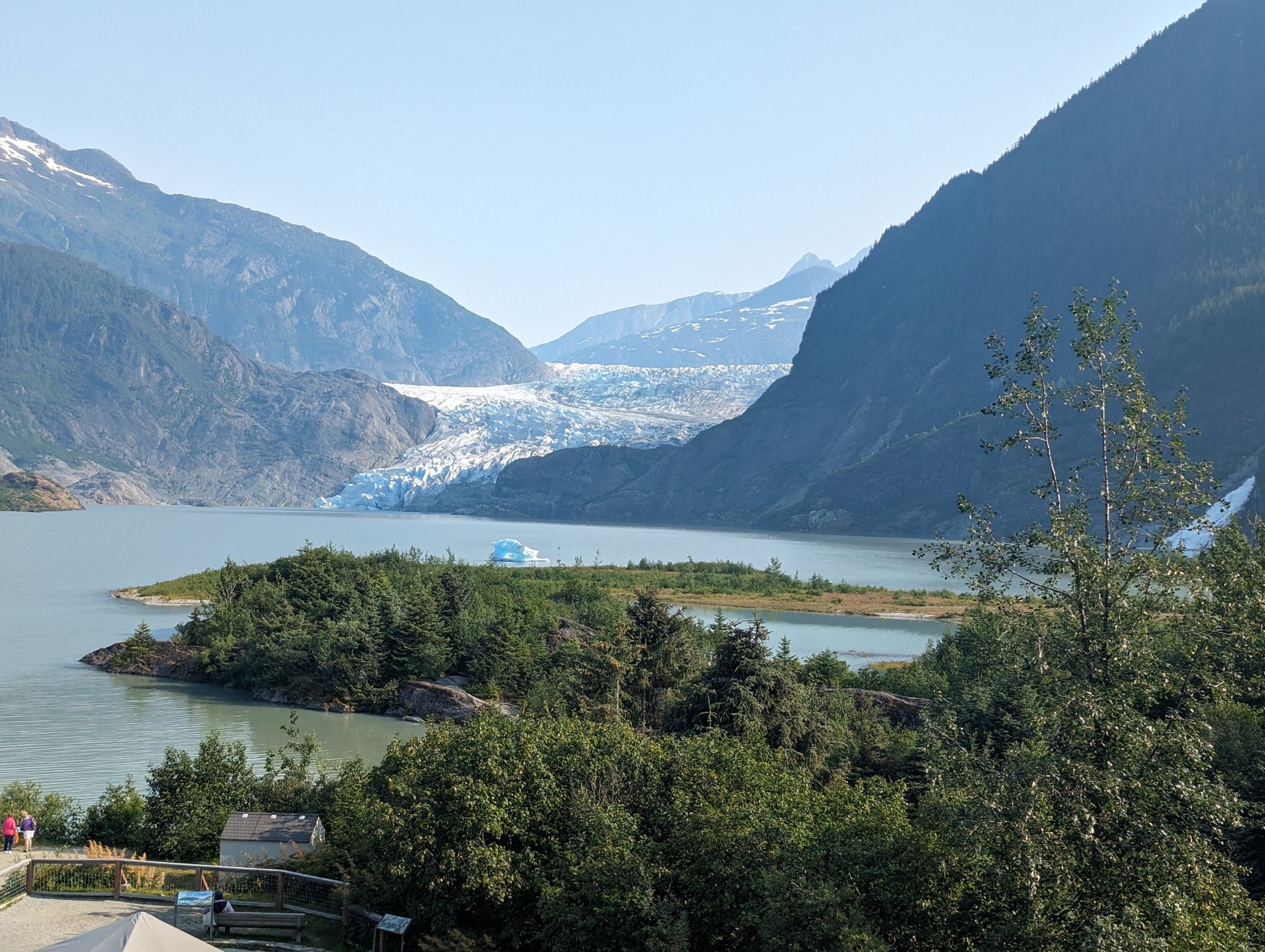 Panoramic view of a large glacier flowing into a lake, surrounded by mountains. - Trail of Time
