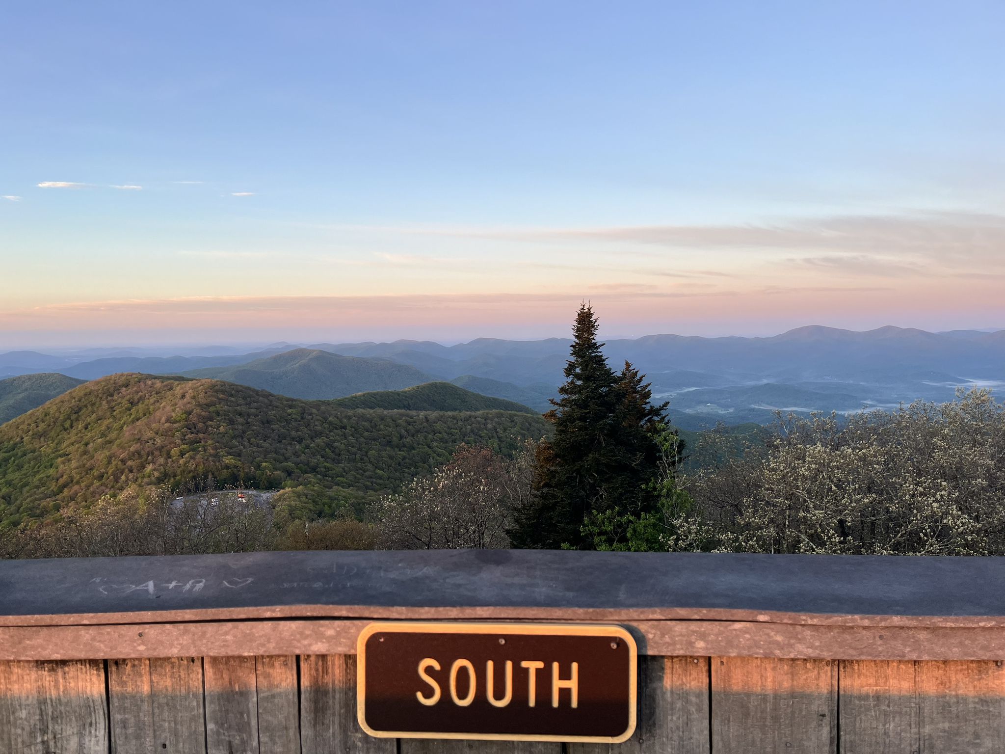 Hazy mountains and a single evergreen tree at twilight, with a 'SOUTH' sign. - Arkaquah Trail
