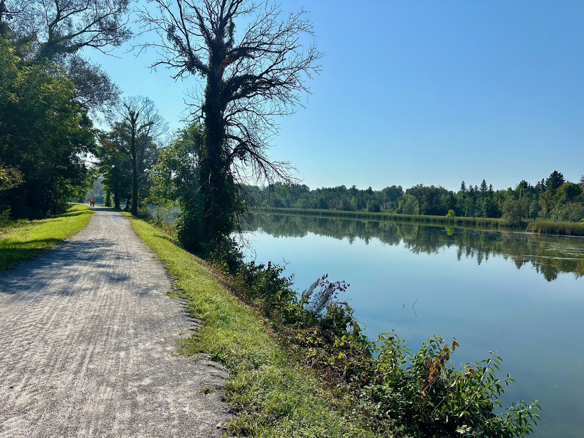 Gravel path alongside a wide river with lush trees under a bright sky. - Erie Canalway Trail – Old Erie Canal Historical Park loop from Green Lakes State Park