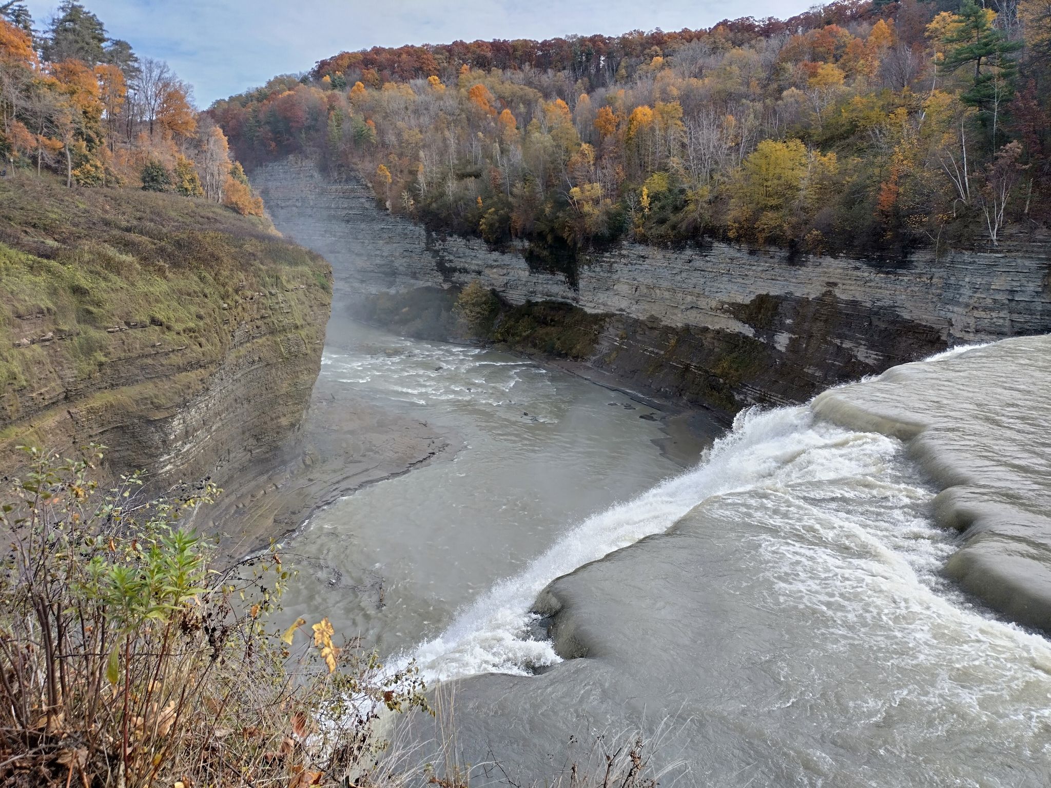 River flowing over a wide waterfall into a rocky gorge with autumn trees. - Hiking loop from Middle Falls