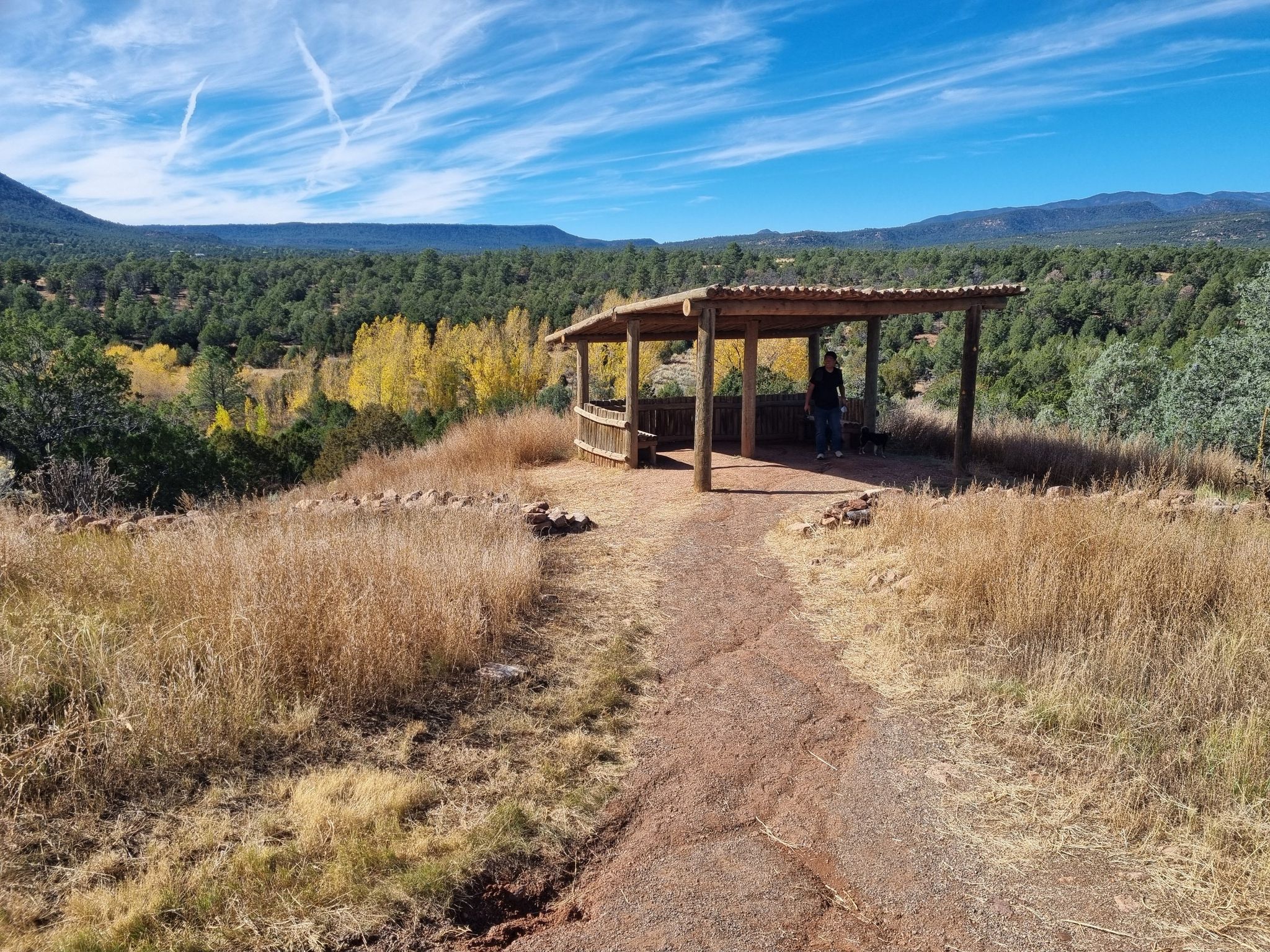 Dirt path leads to a wooden shelter with a person, surrounded by autumn trees. - Ancestral Sites Trail