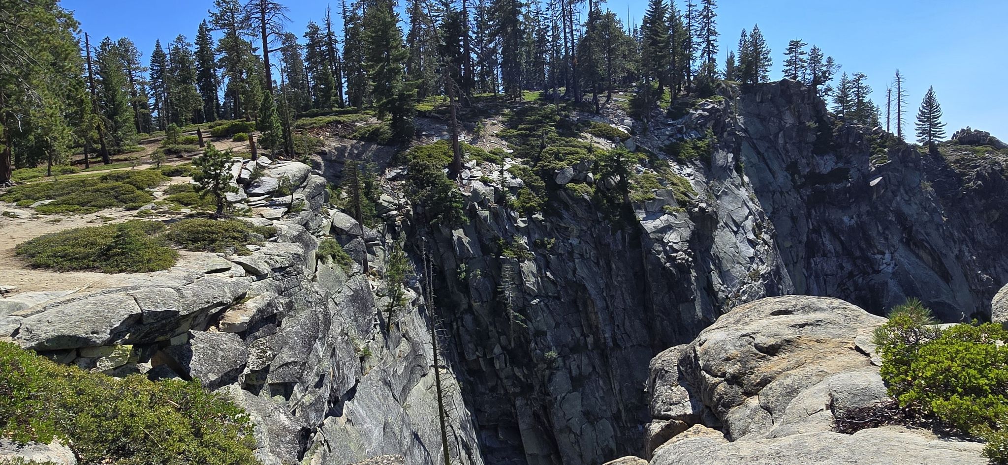 A steep rocky cliff face and surrounding forest under a clear blue sky. - Dewey Point Winter Loop
