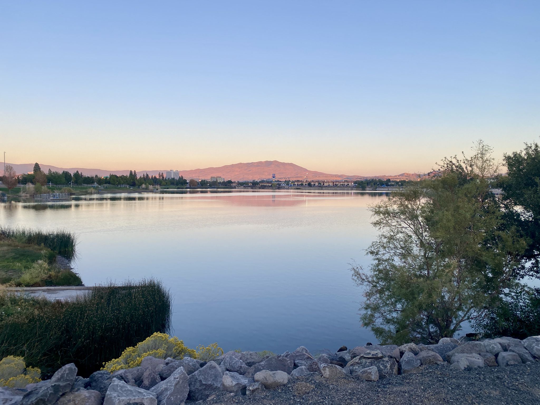 Calm lake reflecting soft sunset light with distant mountains and reeds. - Sparks Marina Loop Trail