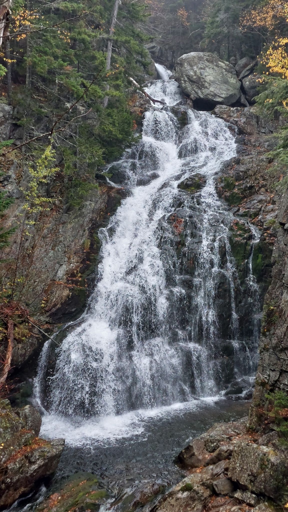 Waterfall cascades down a rocky face surrounded by autumn trees and rocks. - Crystal Cascades