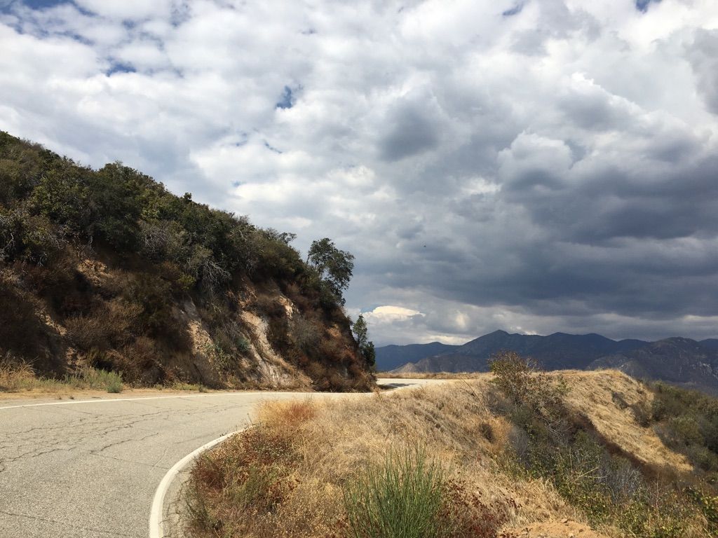 Winding paved road on a dry hillside under a dramatic cloudy sky. - Glendora Ridge Road to Mount Baldy Village loop