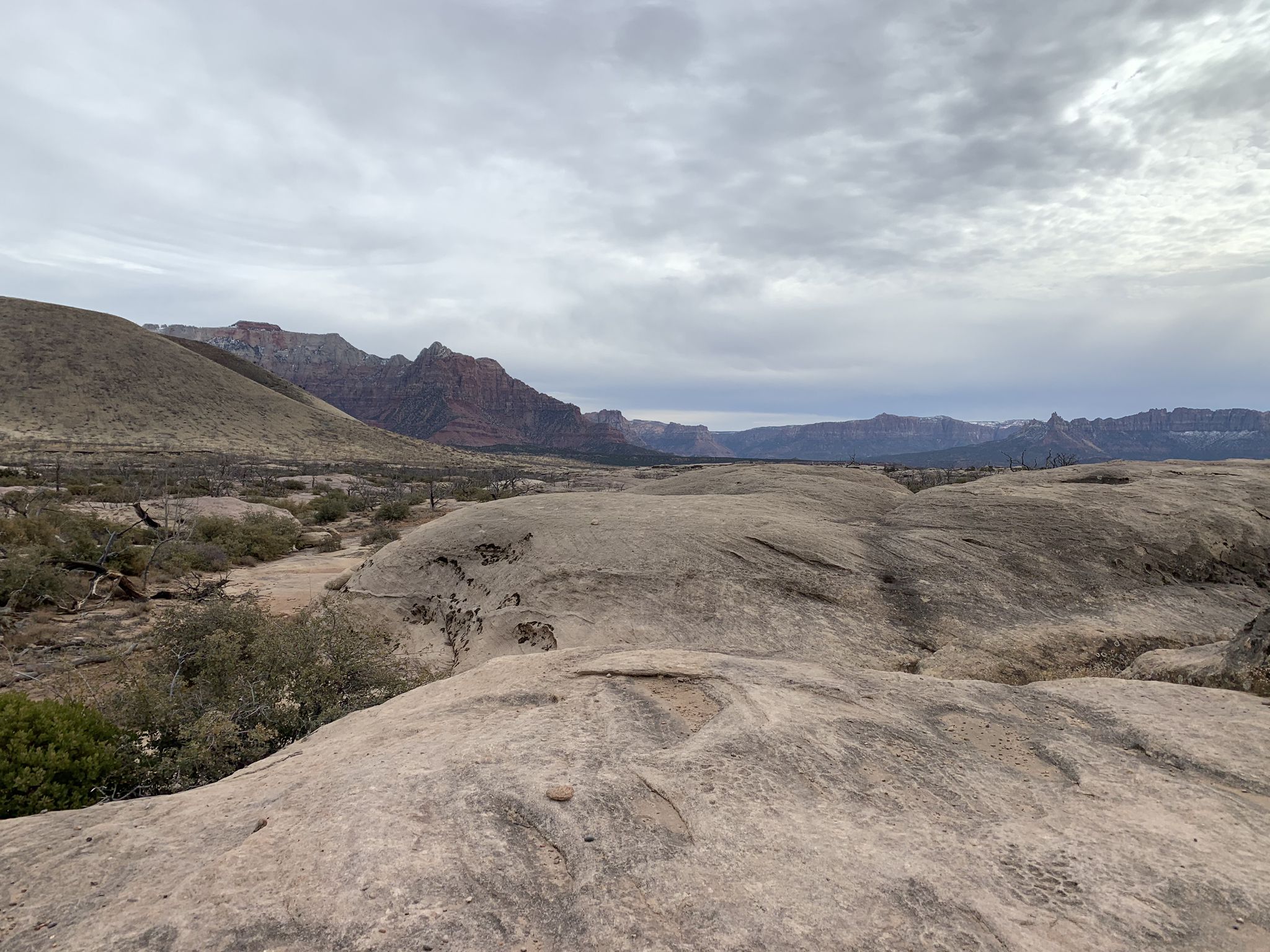 Expansive desert landscape with large rock formations and distant mountains under cloudy sky. - The Whole Guacamole