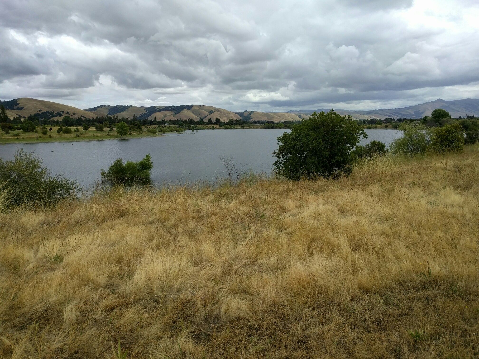 Calm lake surrounded by dry golden grass and distant hills under cloudy sky. - Rainbow Lake loop from Fremont
