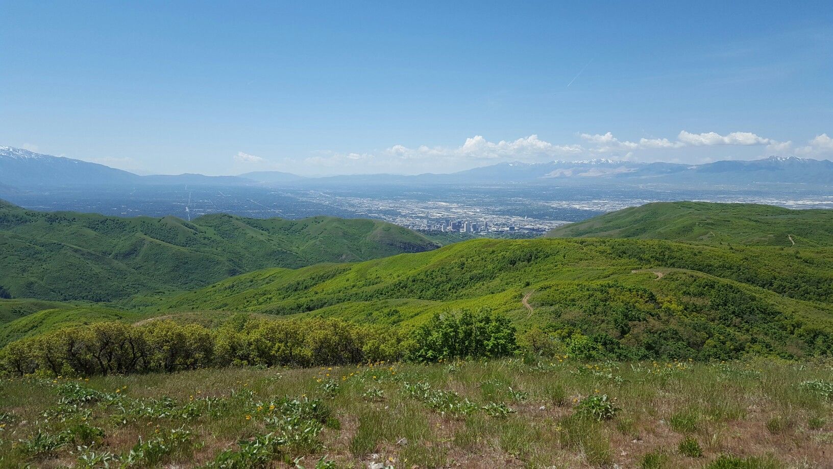 Vast landscape of rolling green hills, distant city, and snow-capped mountains under clear sky. - Dude Benchmark – Grandview Route loop from The Church of Jesus Christ of Latter-day Saints