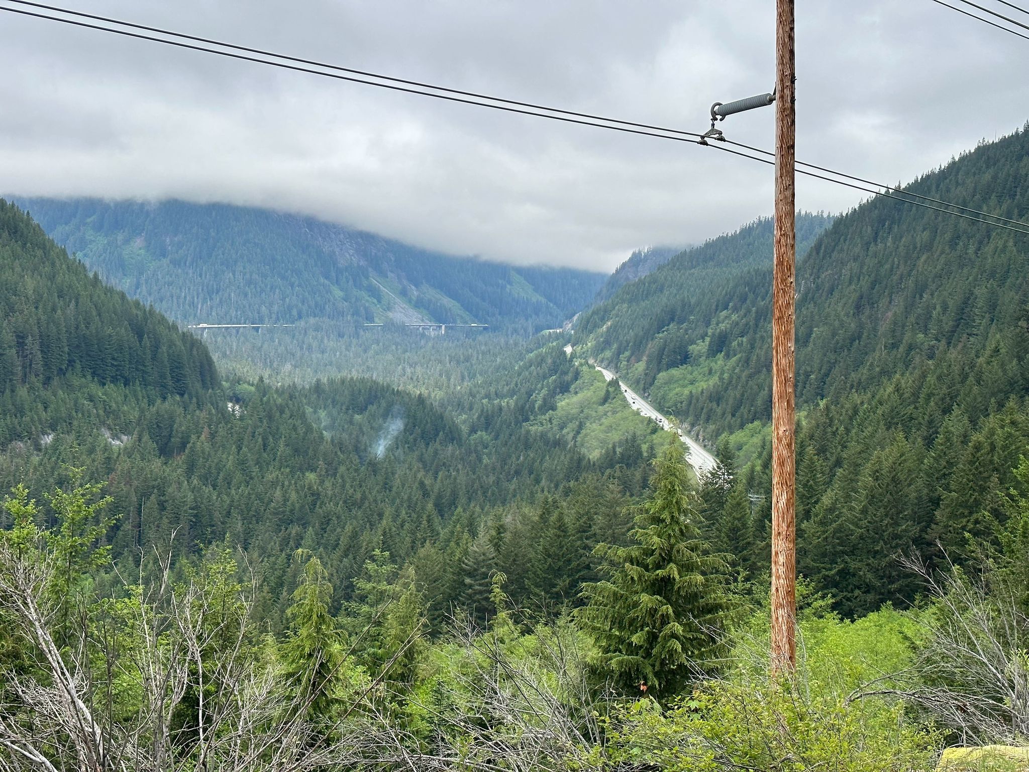 Expansive view of a forested mountain valley with a winding road and power lines. - Snoqualmie Tunnel – Snoqualmie Tunnel loop from Hyak