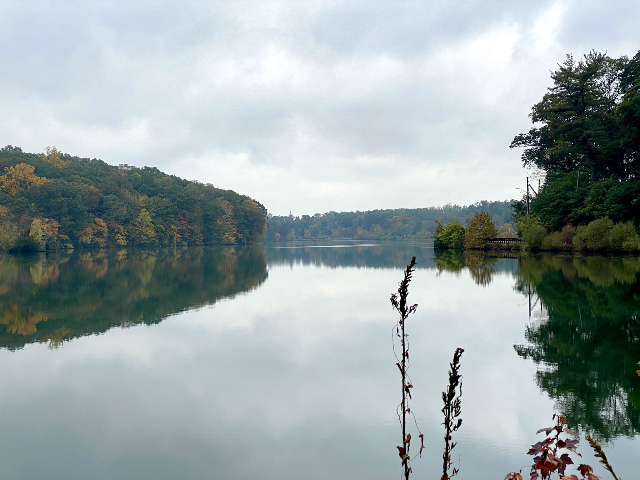 Calm lake reflecting autumn-colored forested hillsides under an overcast sky. - North County Trailway – Eastview Pumping Station loop from Philipse Manor