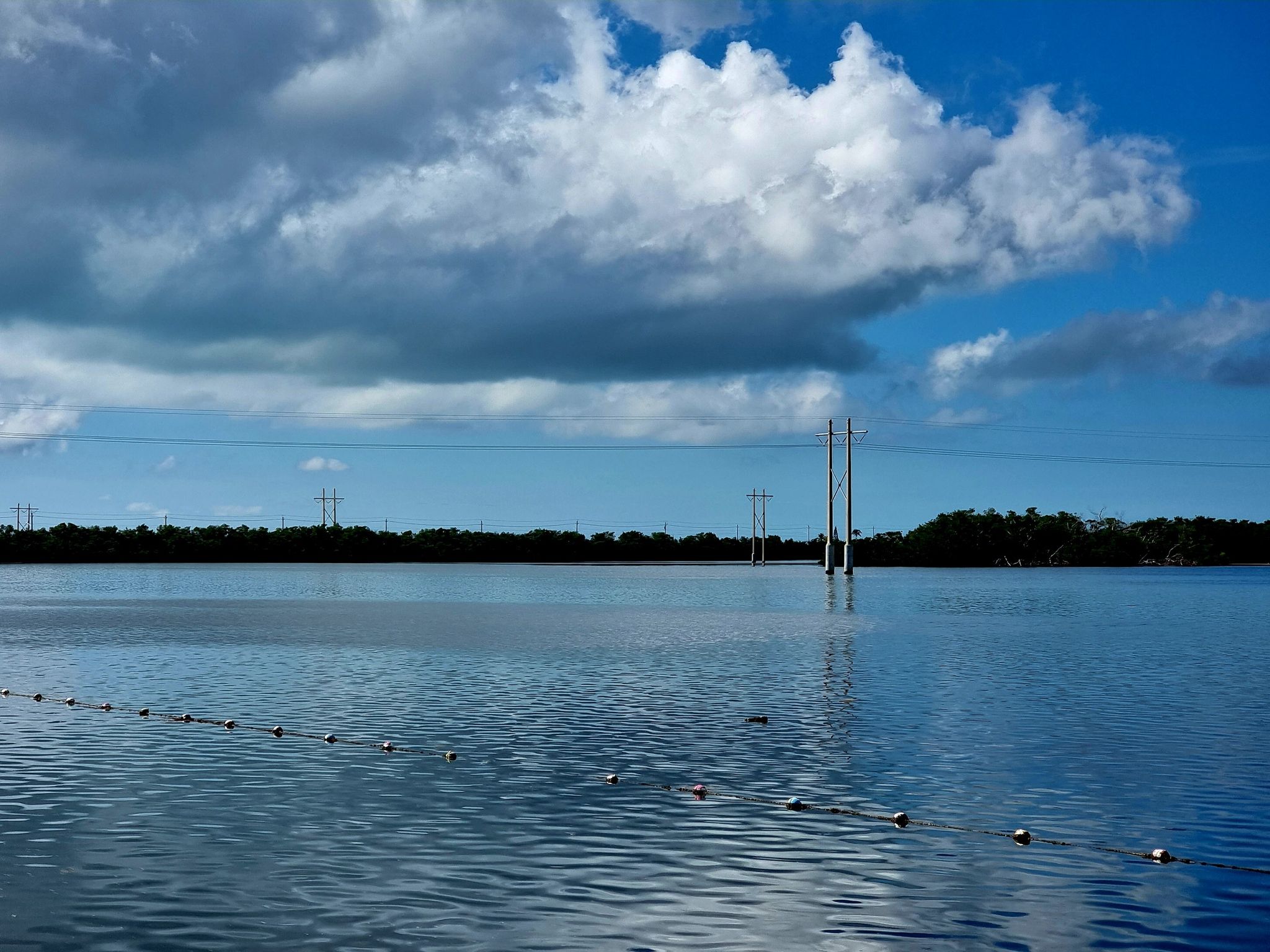 Wide body of water with power lines, distant trees, and cloudy blue sky. - Florida Keys Overseas Heritage Trail