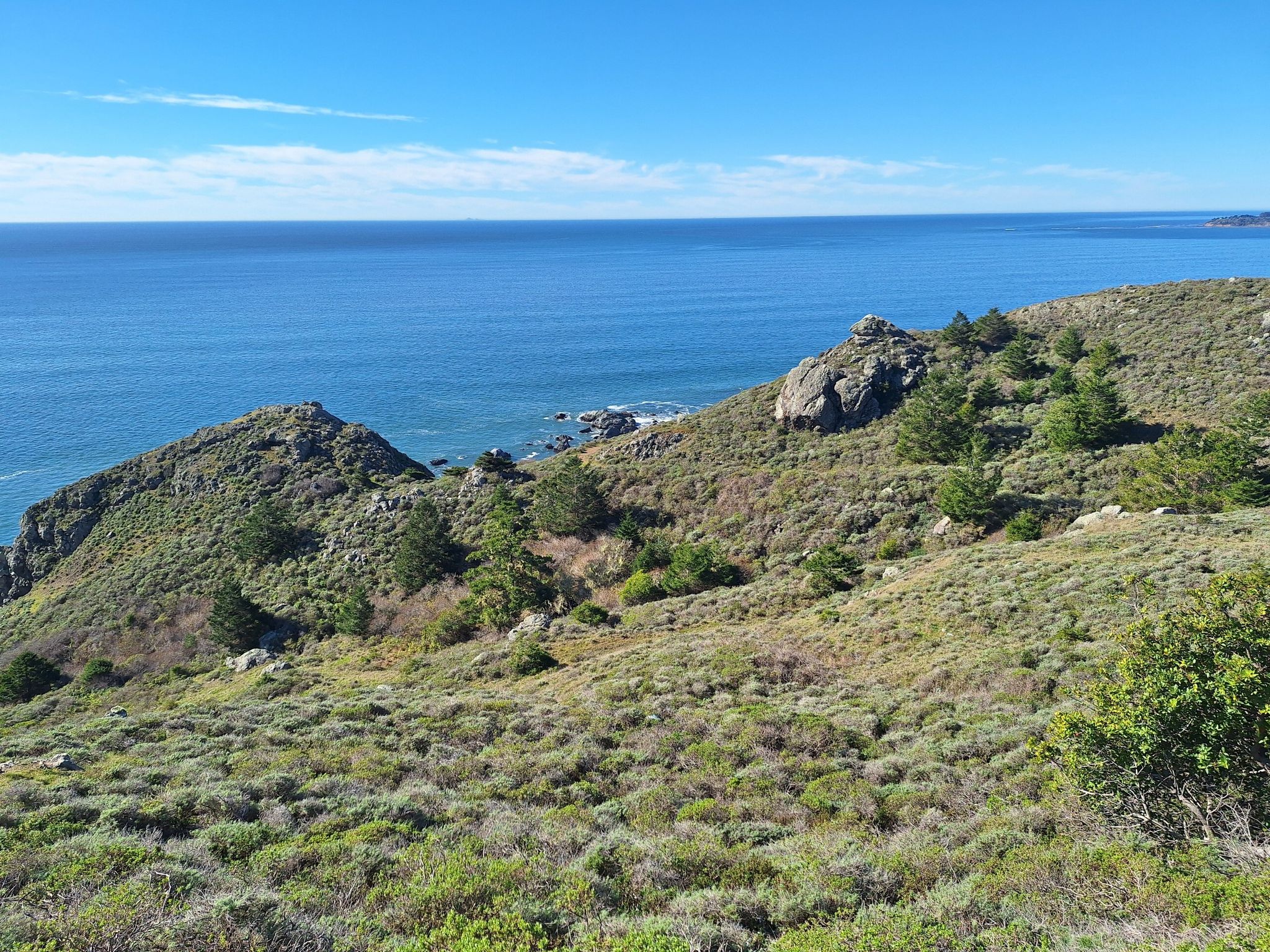 Rocky green hills meet the vast blue ocean on a clear day. - Marin Coastal Bike Route