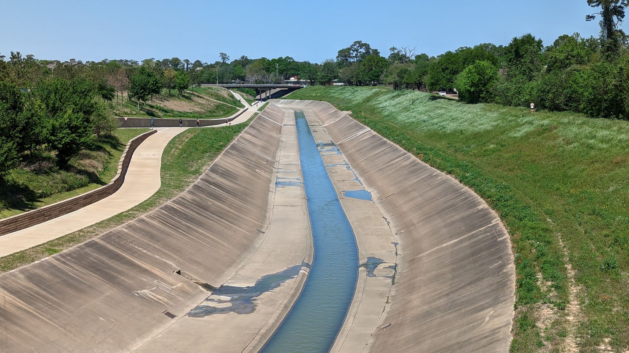 Concrete channel with water, paved path, and green banks under bright sun. - Edith Moore Nature Sanctuary & Memorial Park loop