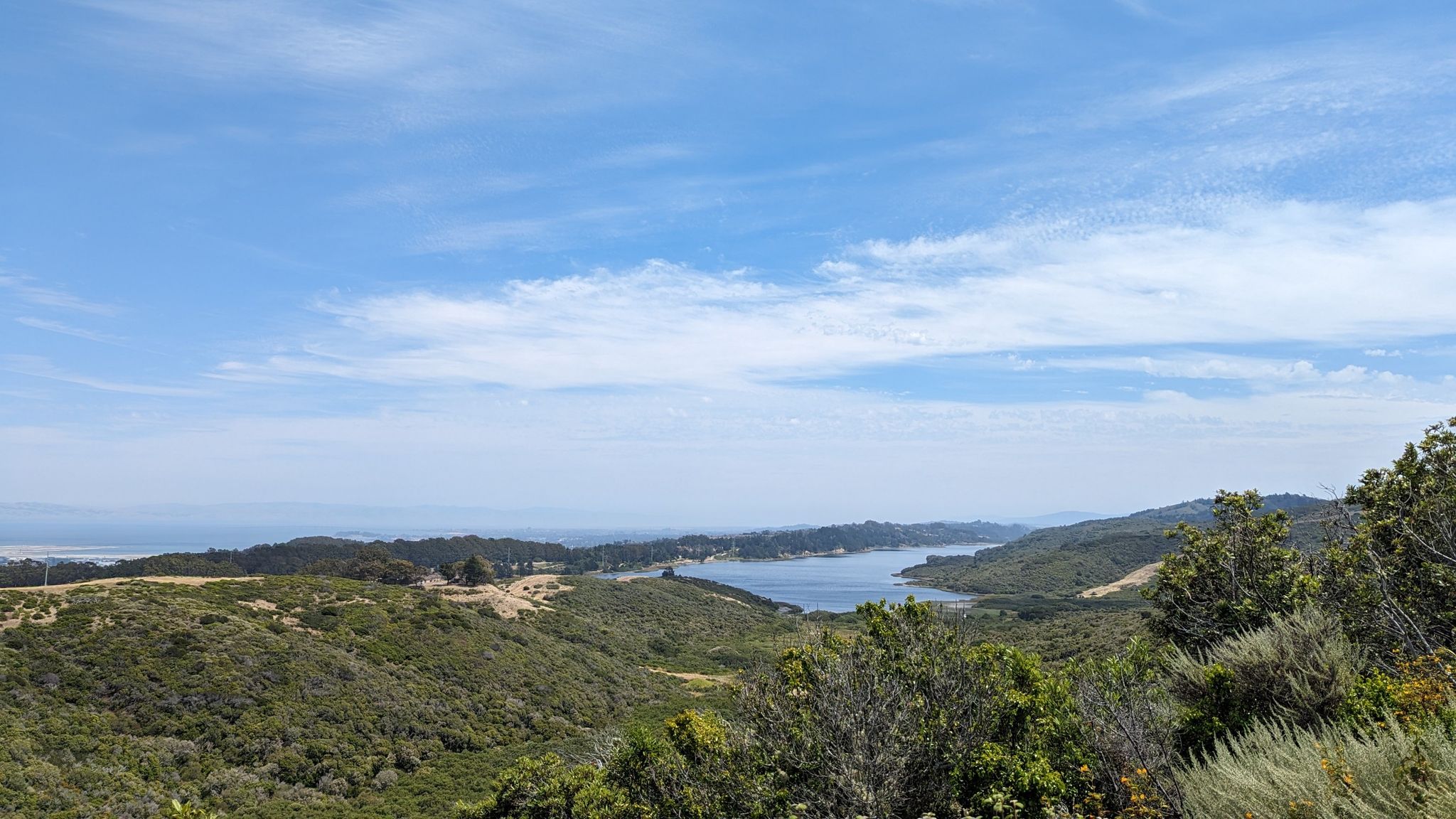 Panoramic view of green hills, a large body of water, and distant ocean. - Sneath Lane Trailhead – Nike Missile Site loop from Sweeney Ridge (GGNRA)