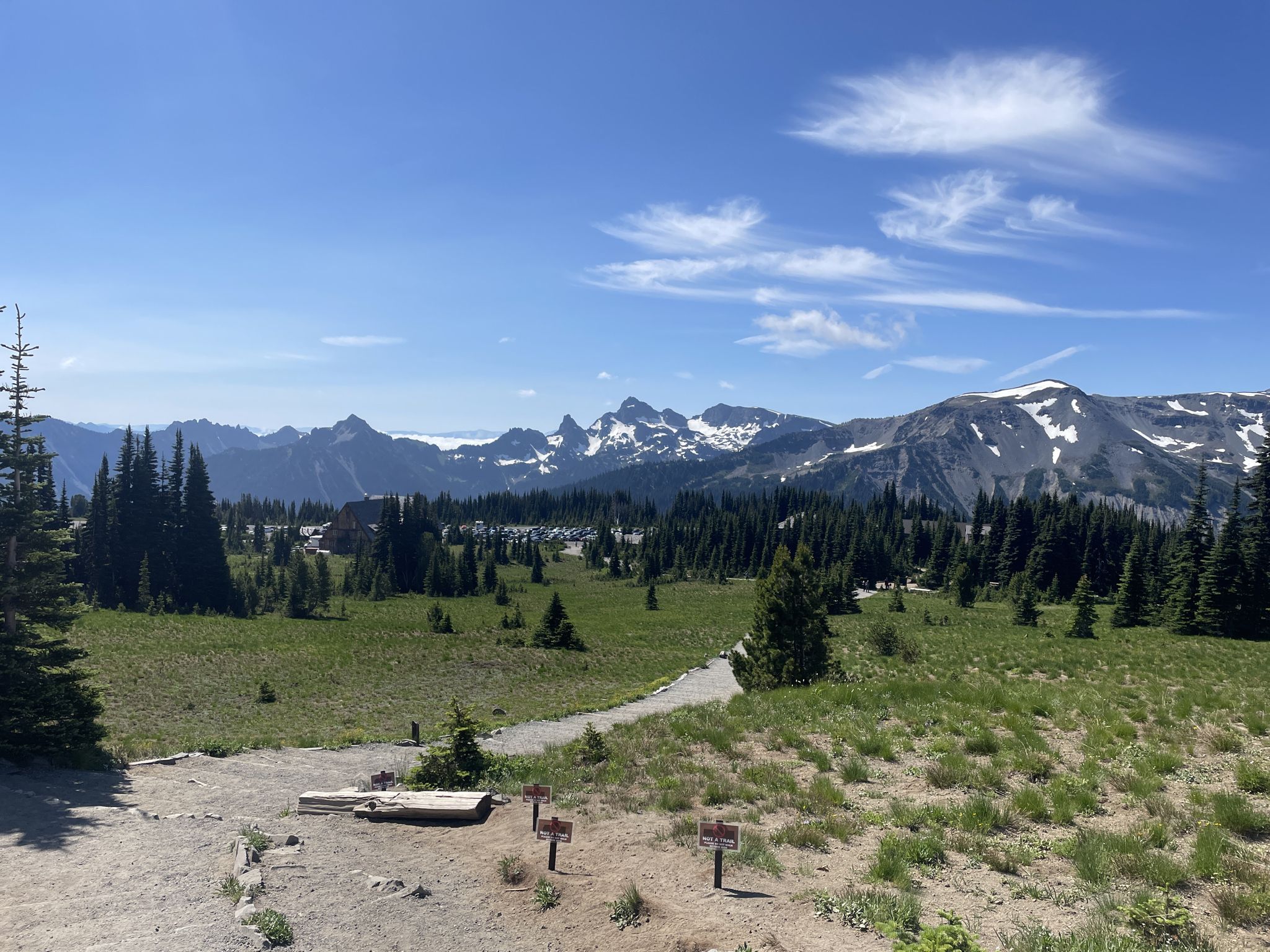 Green meadow with scattered trees, leading to snowy mountains under blue sky. - Sunrise to Mystic Lake