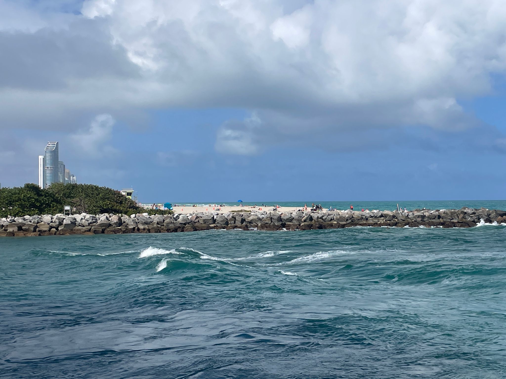 Choppy ocean waves near a rocky jetty with distant city buildings. - Haulover Park – Haulover Inlet loop from Sunny Isles Beach