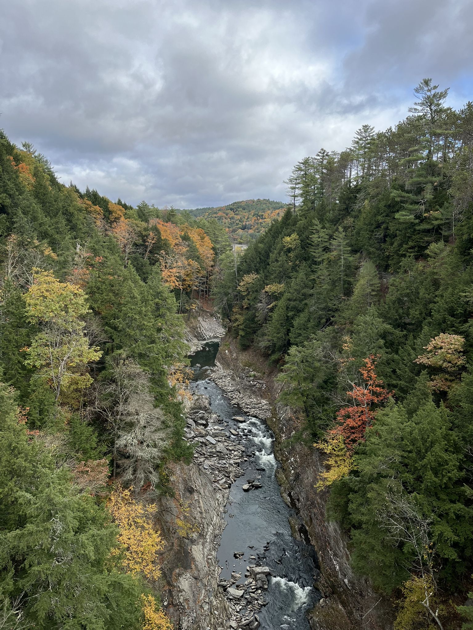 River flows through a rocky gorge with vibrant autumn trees under cloudy sky. - Quechee Gorge Bridge – South Quechee Gorge Overlook loop from Quechee Gorge Bridge