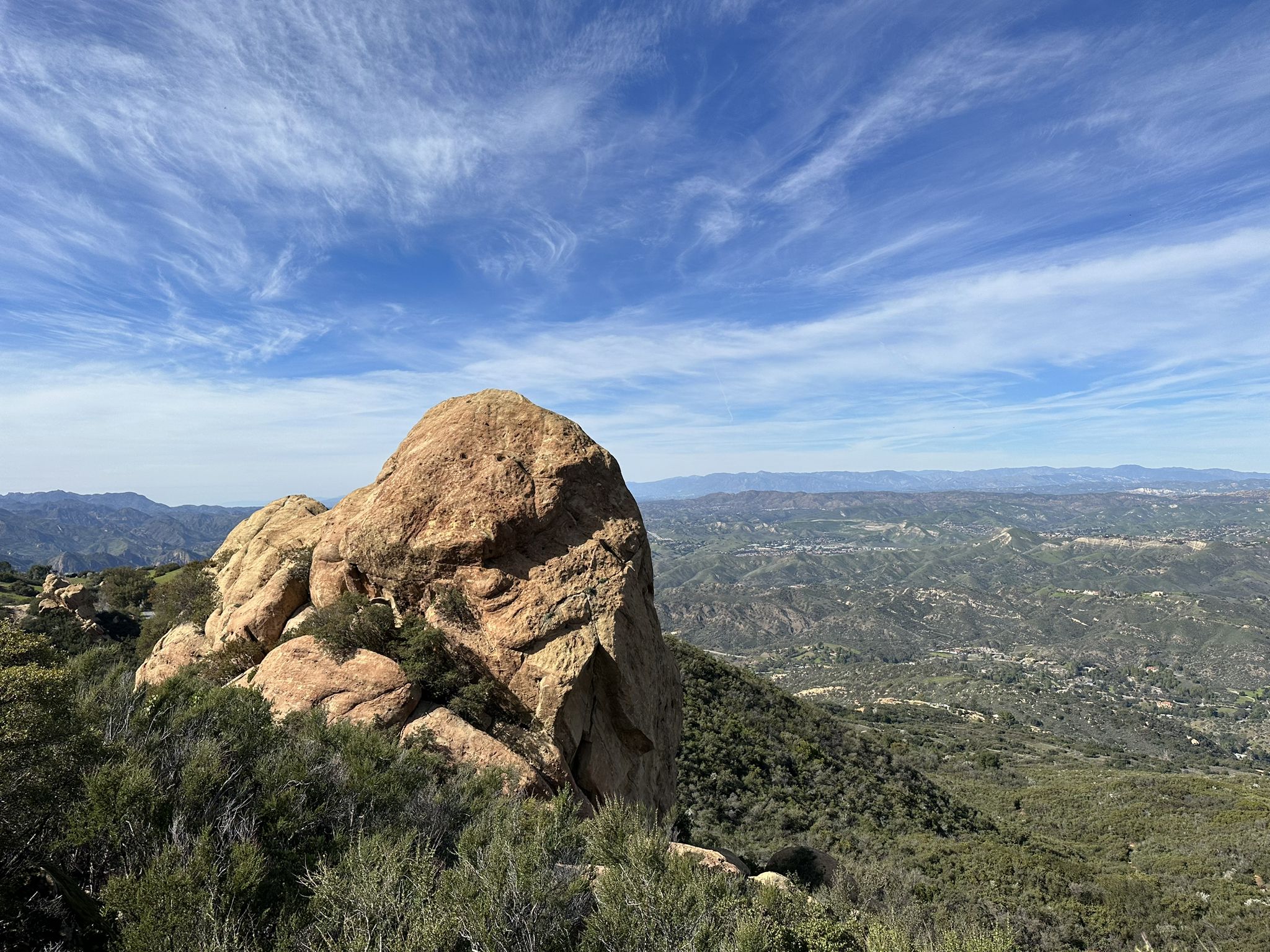Large rock formation on a hill overlooking a green valley under a blue sky. - Backbone Trail Loop