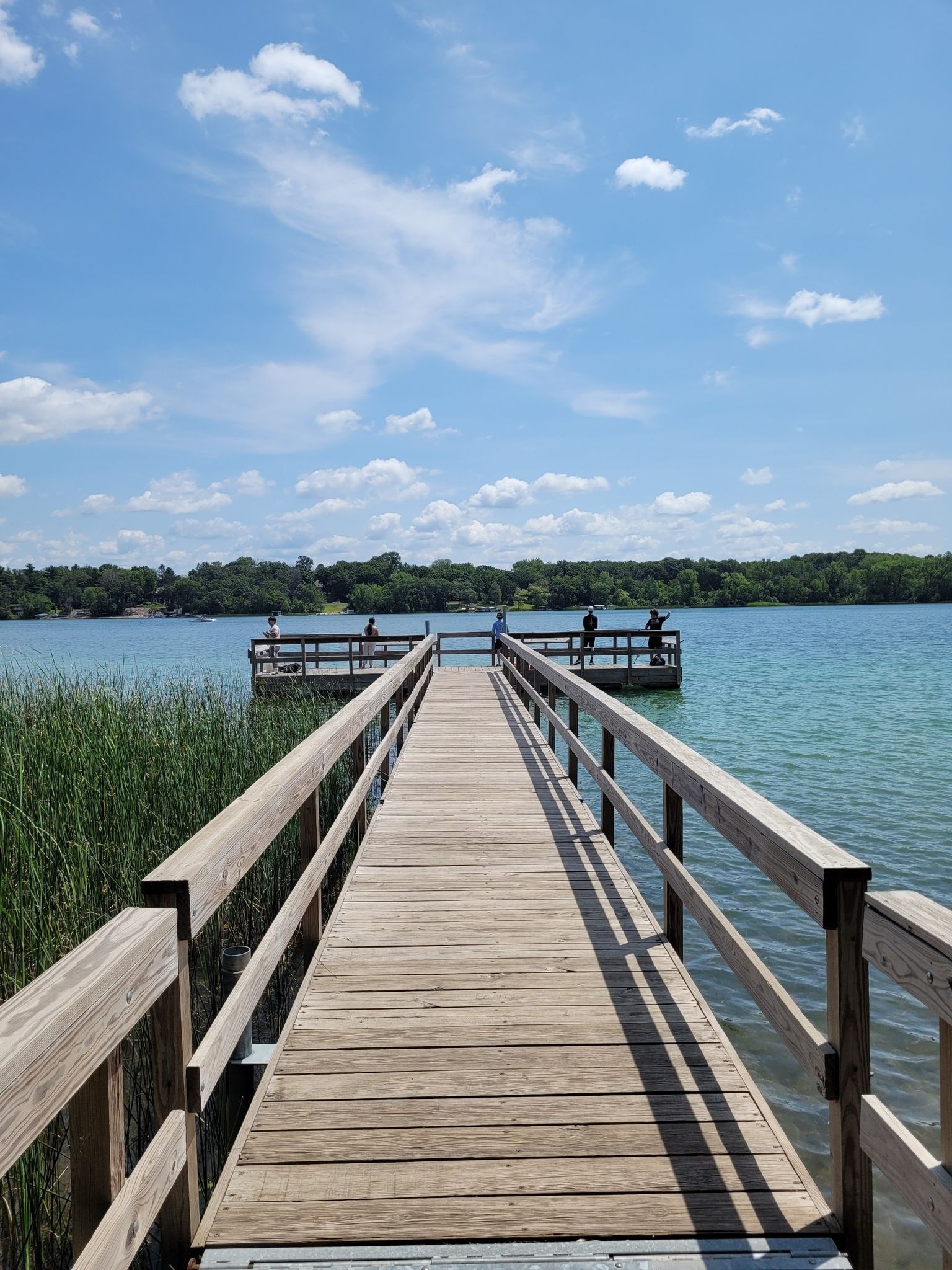 Long wooden pier with people fishing on a sunny lake with blue sky. - Lake Elmo Paved Trail