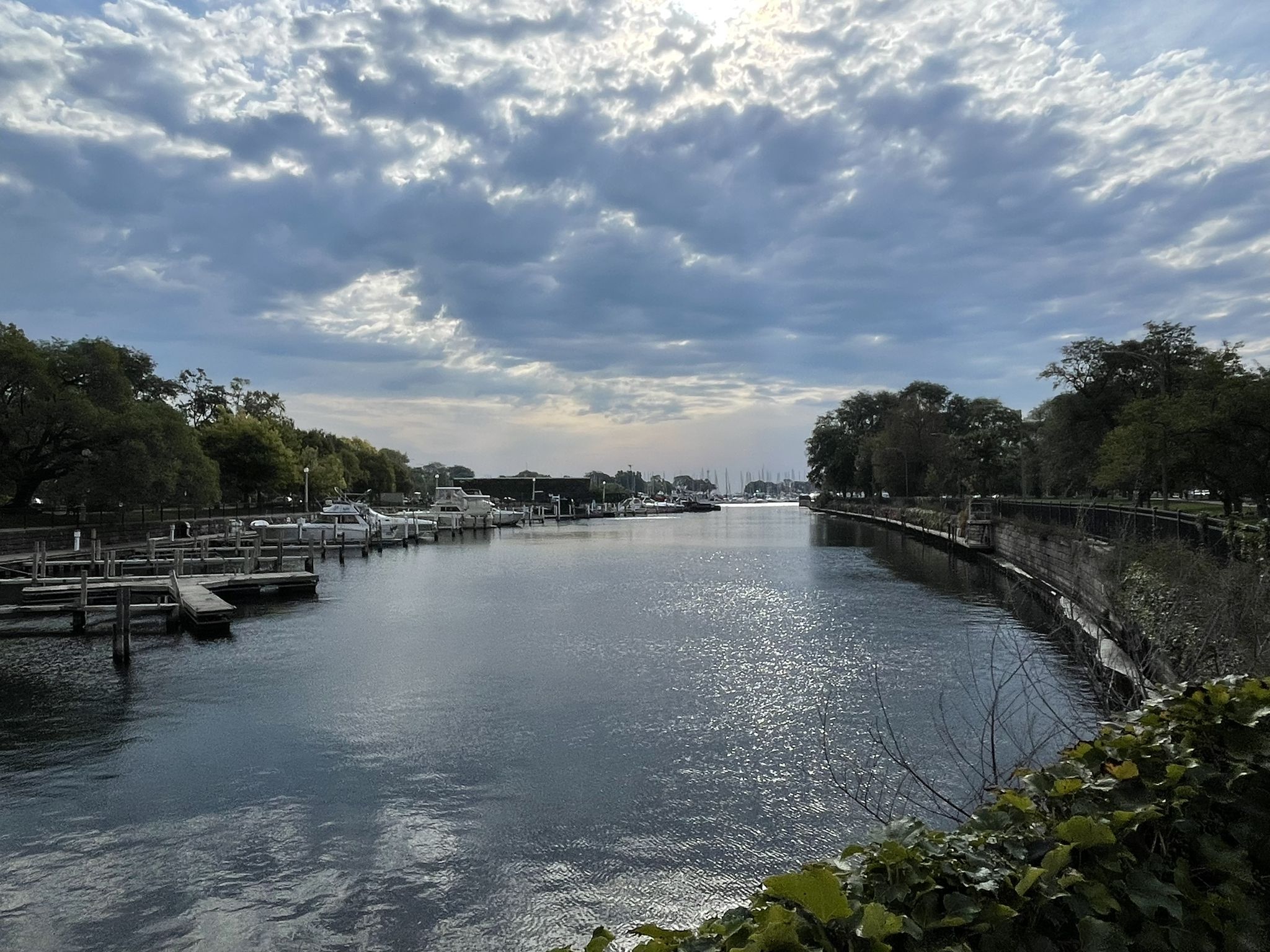 A wide waterway with docks and trees under a bright, cloudy sky. - Lakefront Trail