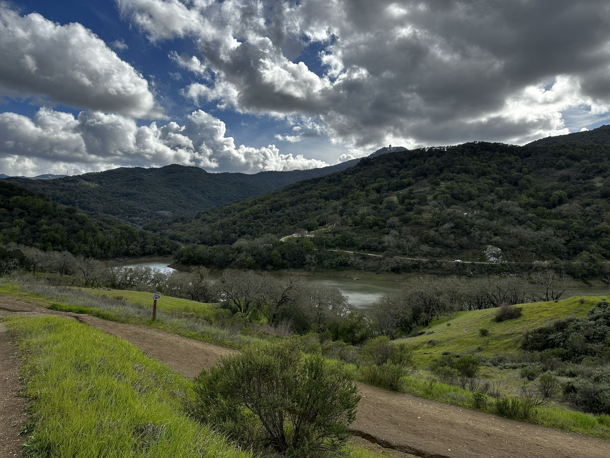 Dirt path overlooking a lake and forested hills under dramatic cloudy sky. - Randol and New Almaden Trail Loop