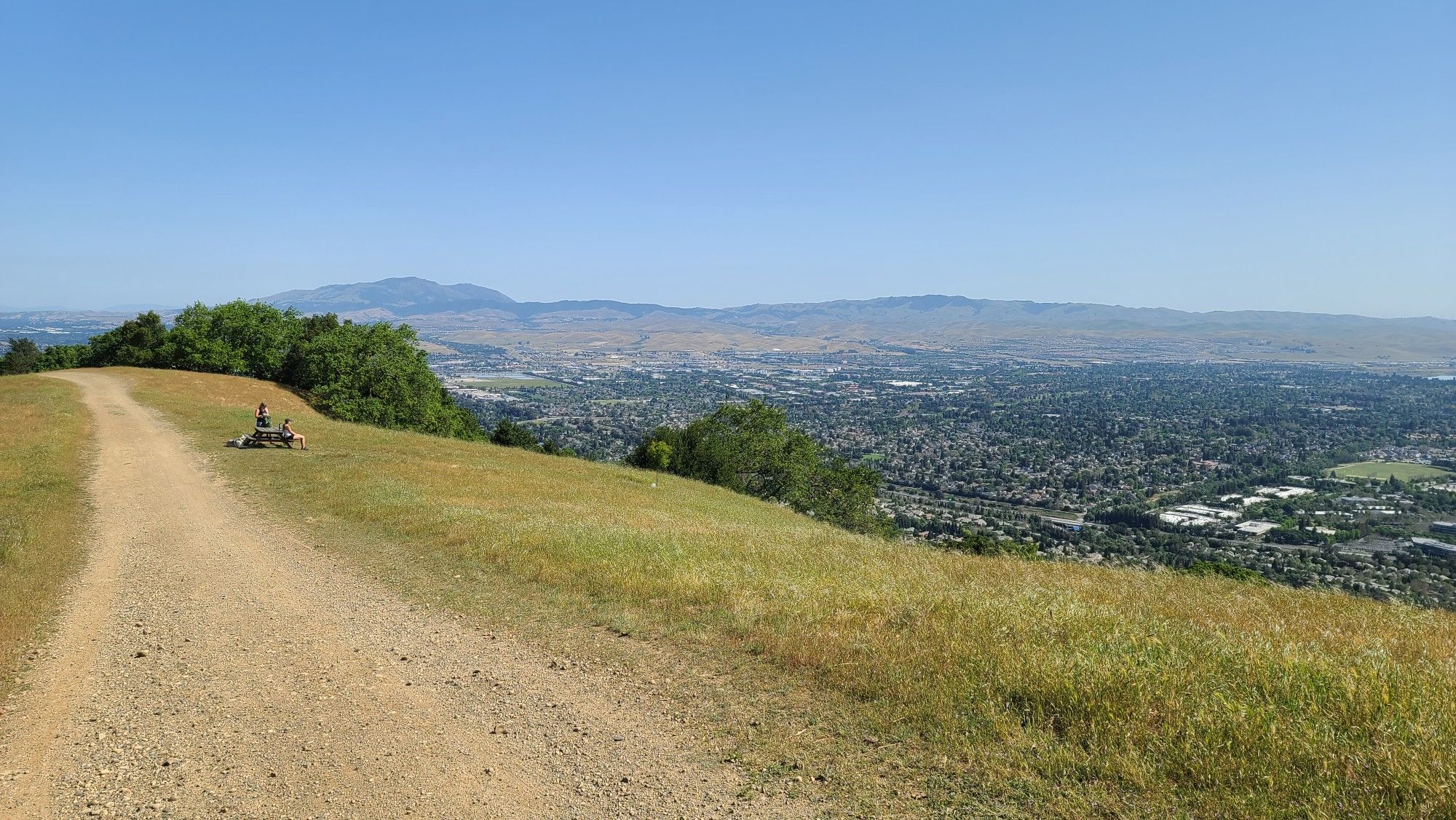 A dirt path on a grassy hill overlooks a sprawling city and distant mountains. - Ridgeline and Thermalito Trail Loop