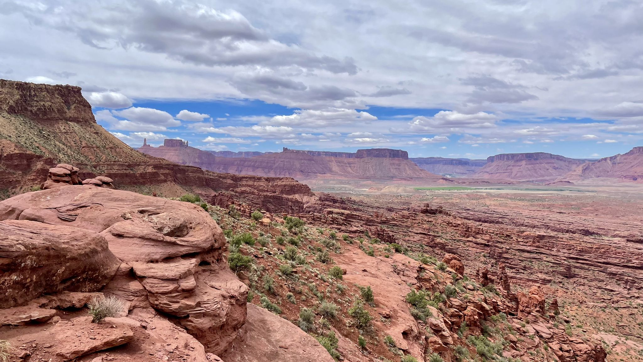 Expansive red rock canyon landscape with sparse vegetation under a partly cloudy sky. - Fisher Towers Trail