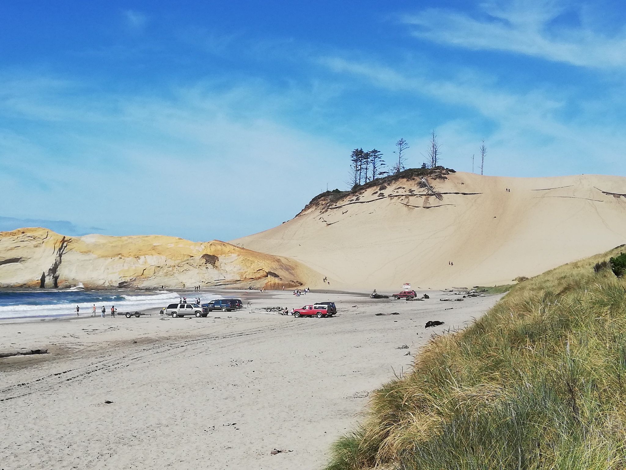 Sunny beach with large sand dune, ocean waves, and parked vehicles. - Cape Kiwanda State Natural Area