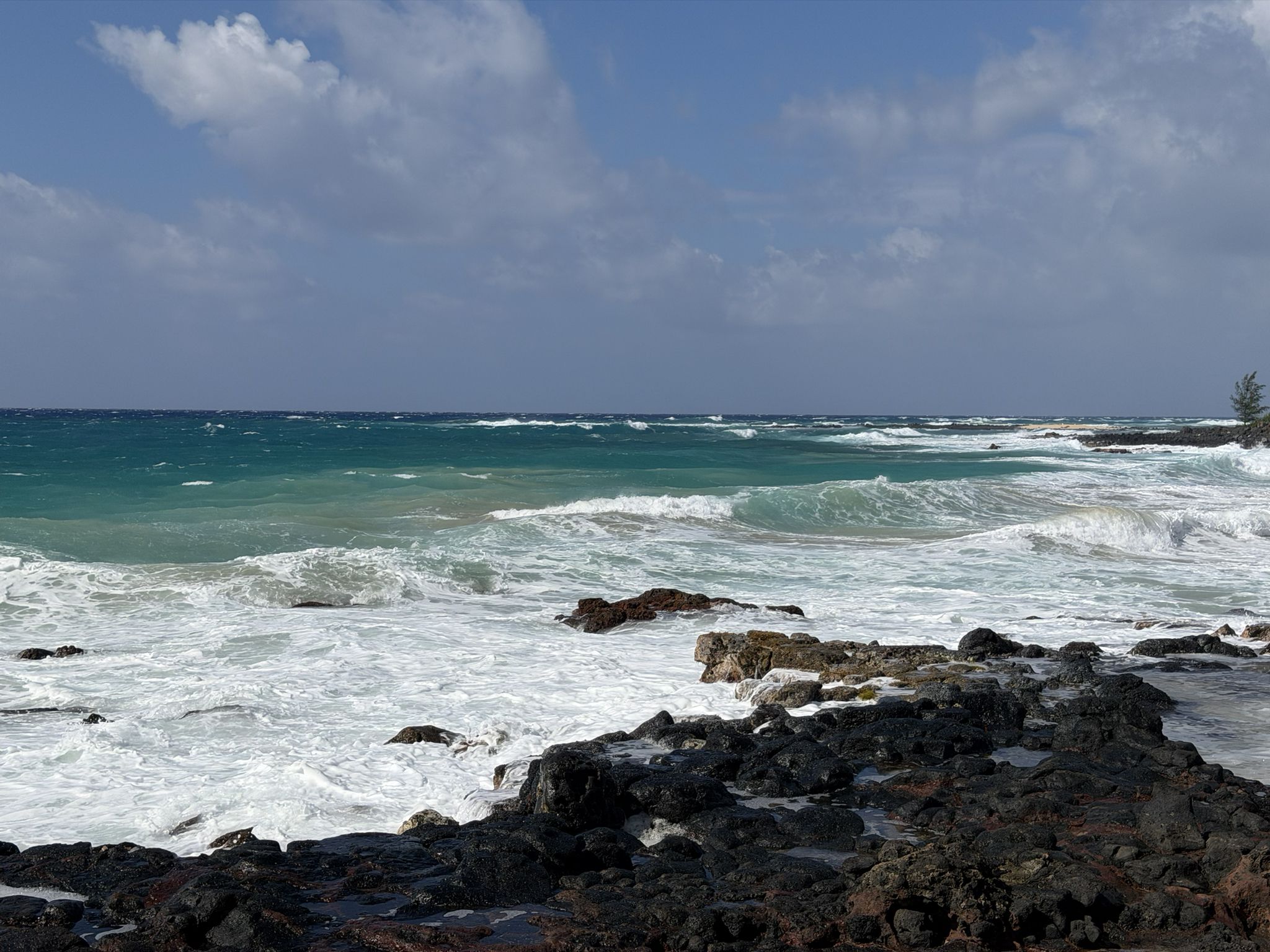 Rough turquoise ocean waves crashing on dark volcanic rocks under a blue sky. - Koloa Heritage Trail and Poipu Loop