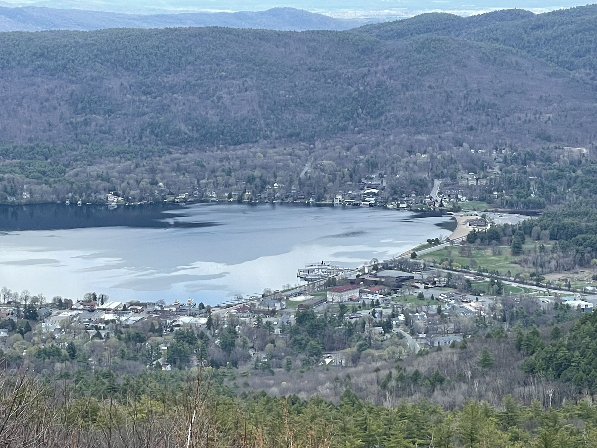 Aerial view of a lake, town, and forested mountains under an overcast sky. - Prospect Mountain Trail