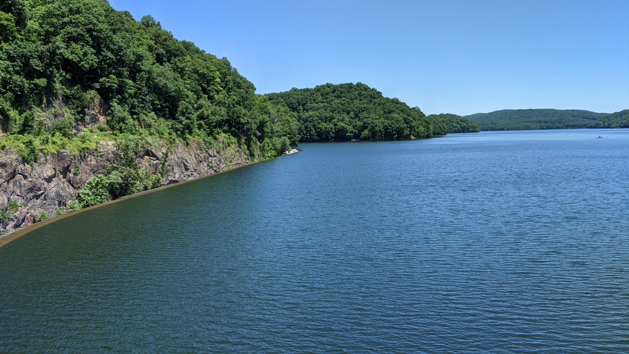 Blue lake with a rocky, forested shoreline under a clear sky. - New Croton Dam – Old Croton Dam Road Bridge loop from Croton-Harmon