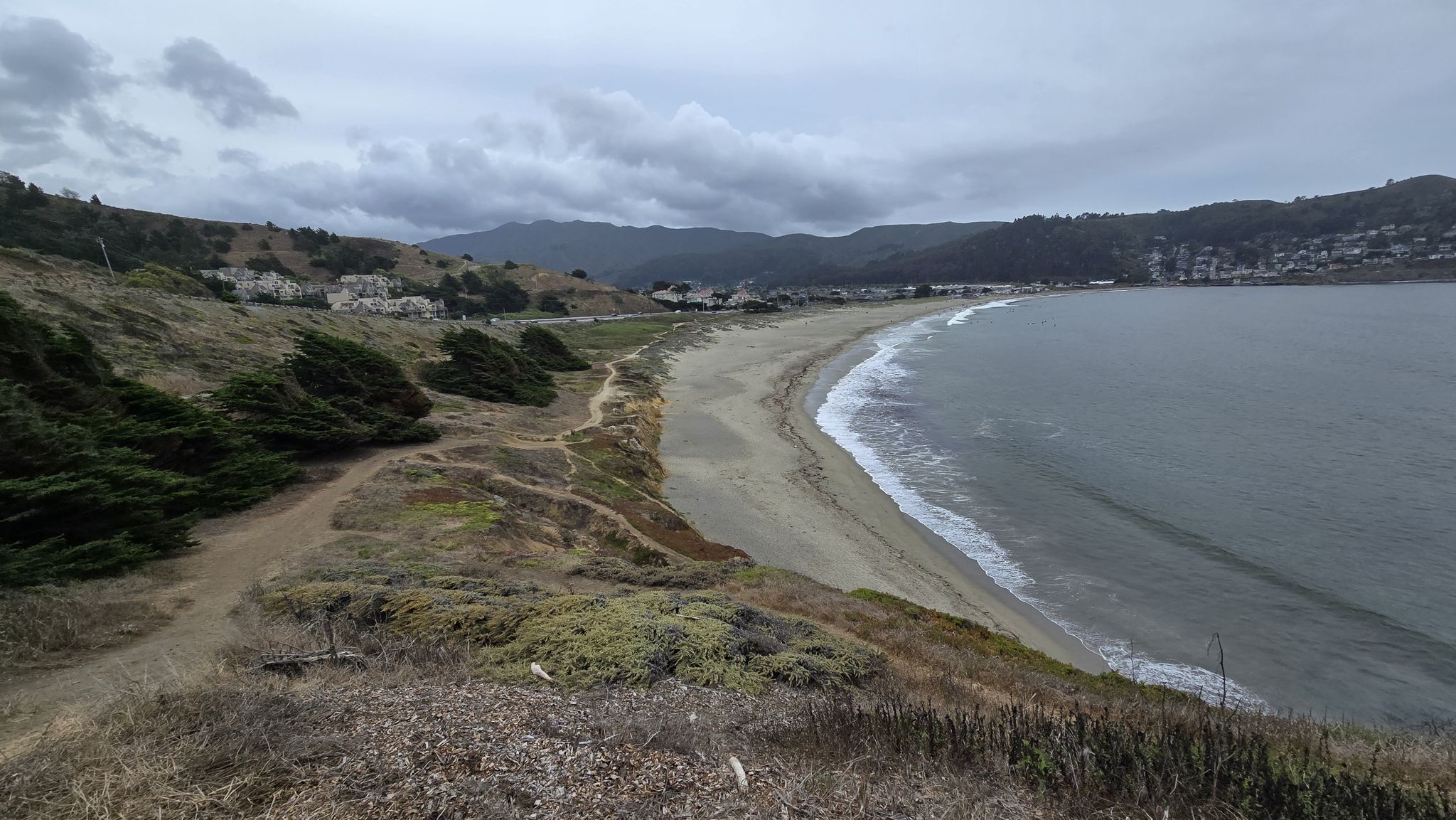 Overcast view of a wide sandy beach, ocean, and distant hills. - Pacific Coast Bike Route: Daly City to Montara