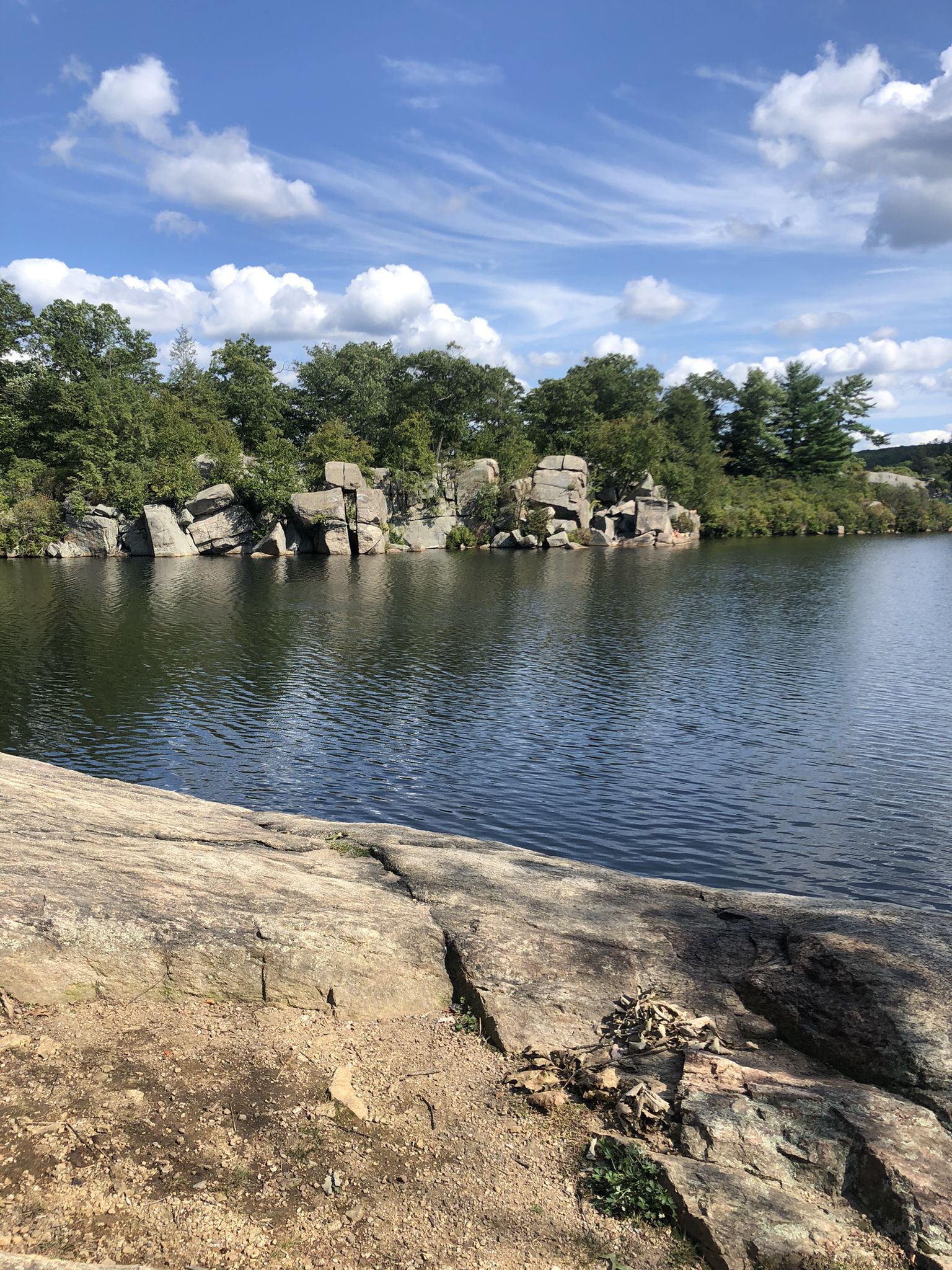 Clear lake with rocky cliffs and green trees under a bright, cloudy sky. - Stony Brook Trail – Pine Meadow Lake loop from Reeves Meadow Visitors Center