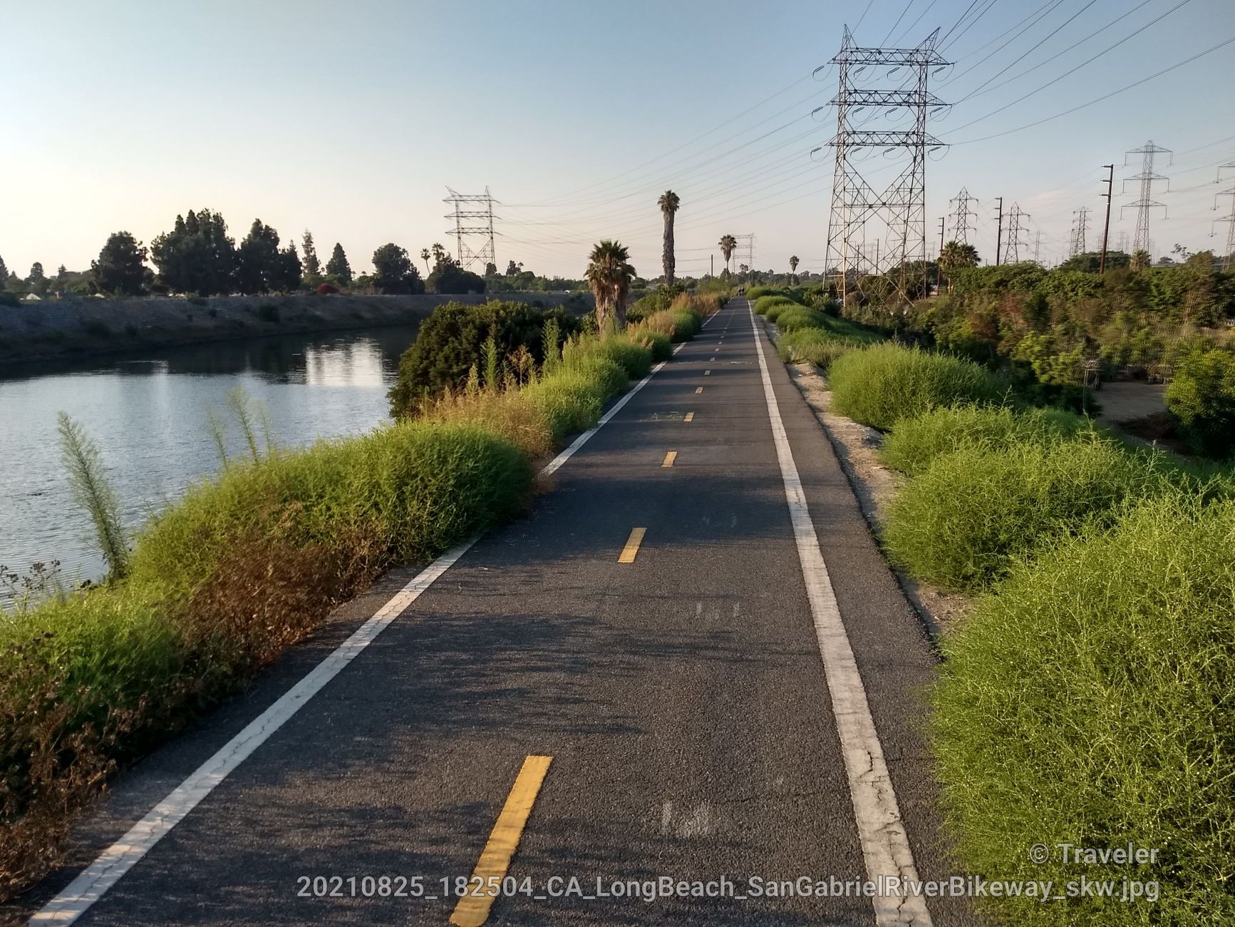 Paved path alongside a river, with green bushes and power lines. - San Gabriel River Trail – San Gabriel River Trail loop from California State University, Long Beach