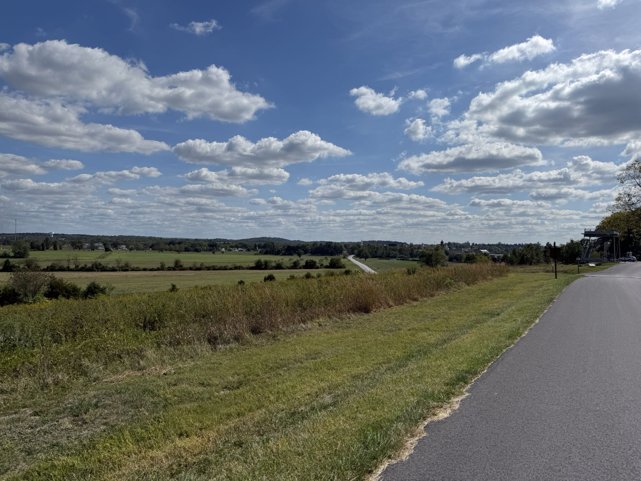Paved road beside green fields under a bright, cloudy sky. - Michaux State Forest – Jennie Wade House loop from Gettysburg & Harrisburg Railroad Depot