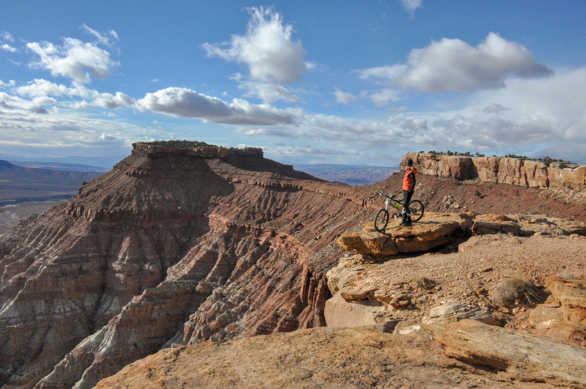 Mountain biker stands on a red rock cliff overlooking a vast canyon. - Gooseberry Mesa – MTB Trails in Hurricane, Utah