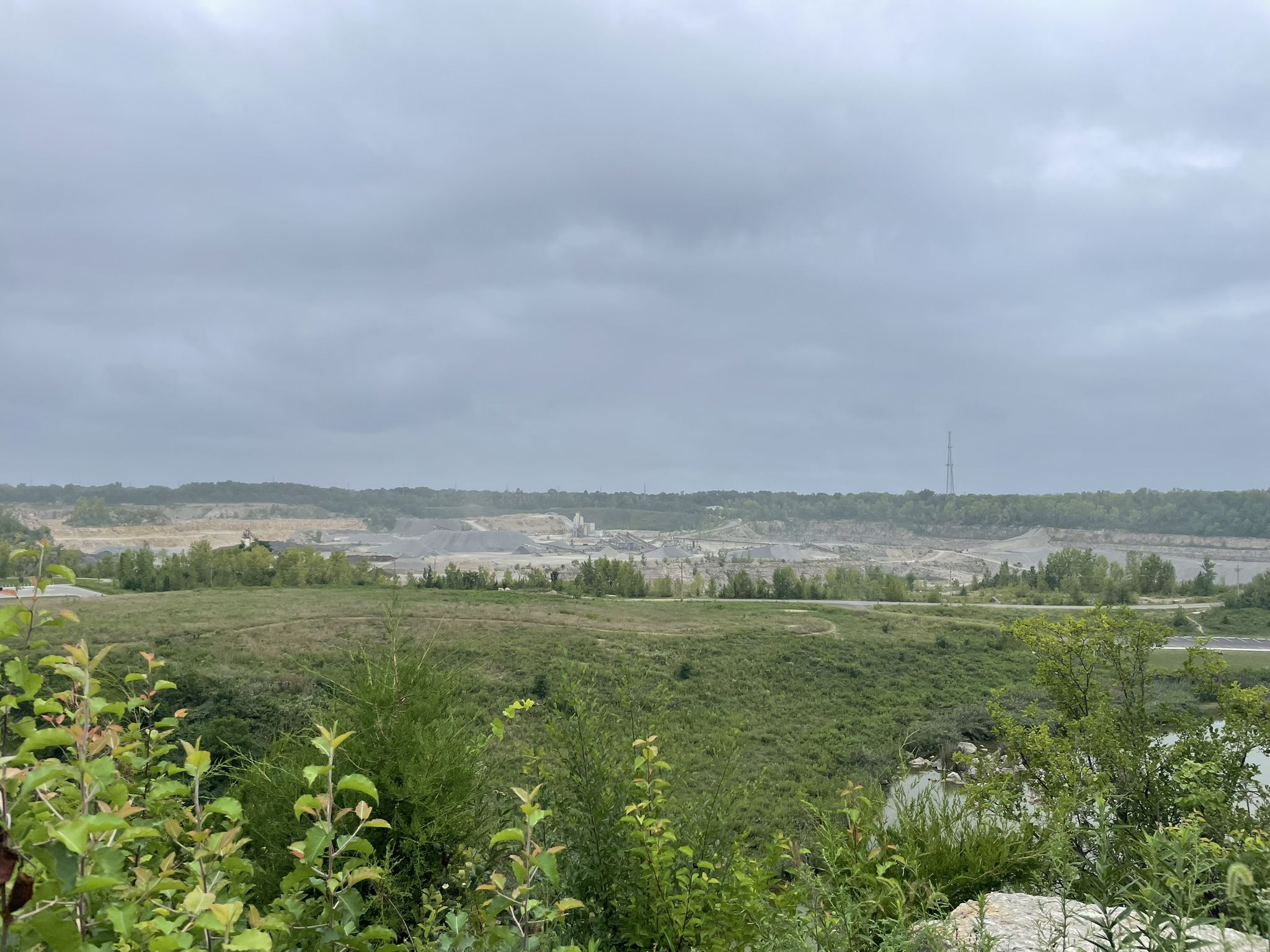 Overcast view of a distant industrial area beyond green fields. - Roberts Millikin Ditch loop from Quarry Trails Metro Park