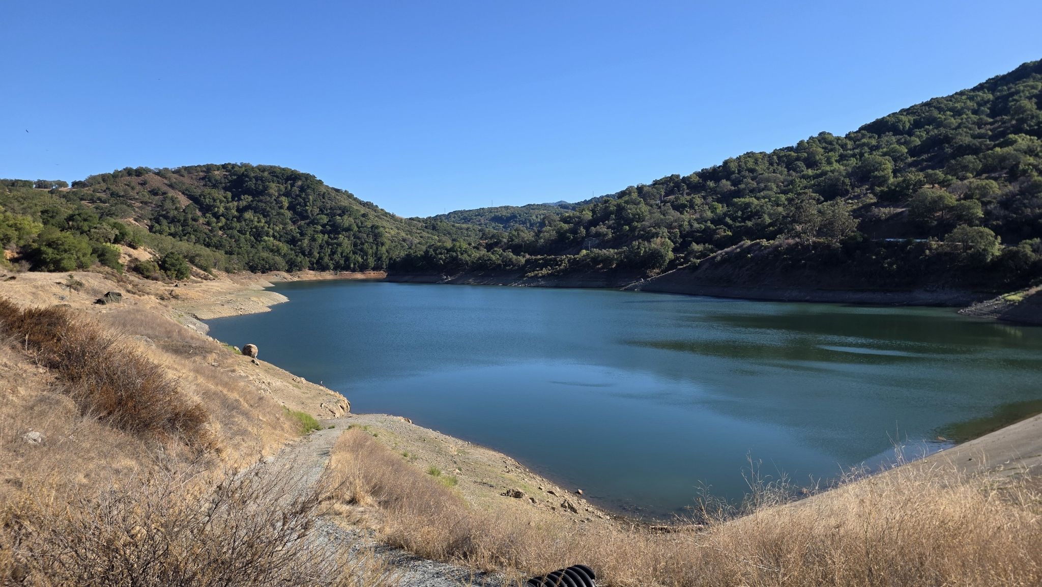A blue lake surrounded by dry and green forested hills under a clear sky. - Guadalupe and Mine Hill Trail Loop