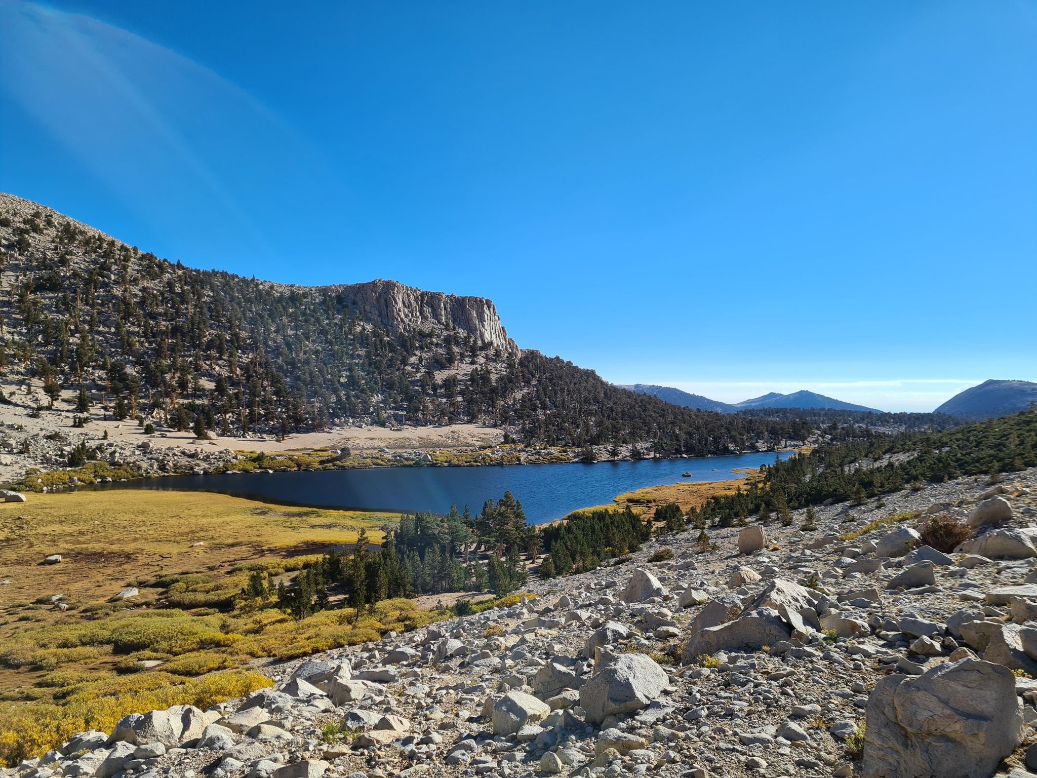 Clear blue lake nestled among rocky mountains and golden grass on a sunny day. - Cottonwood Lakes and Army Pass Loop
