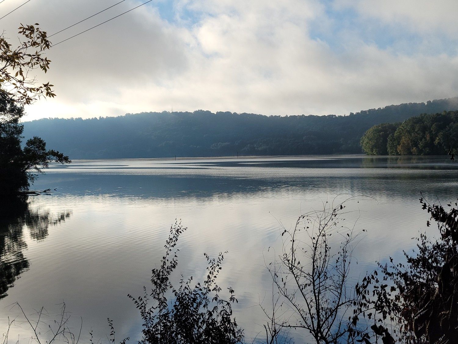 A calm lake reflecting a cloudy sky, with dark forested shores. - Haw Ridge Park Loop