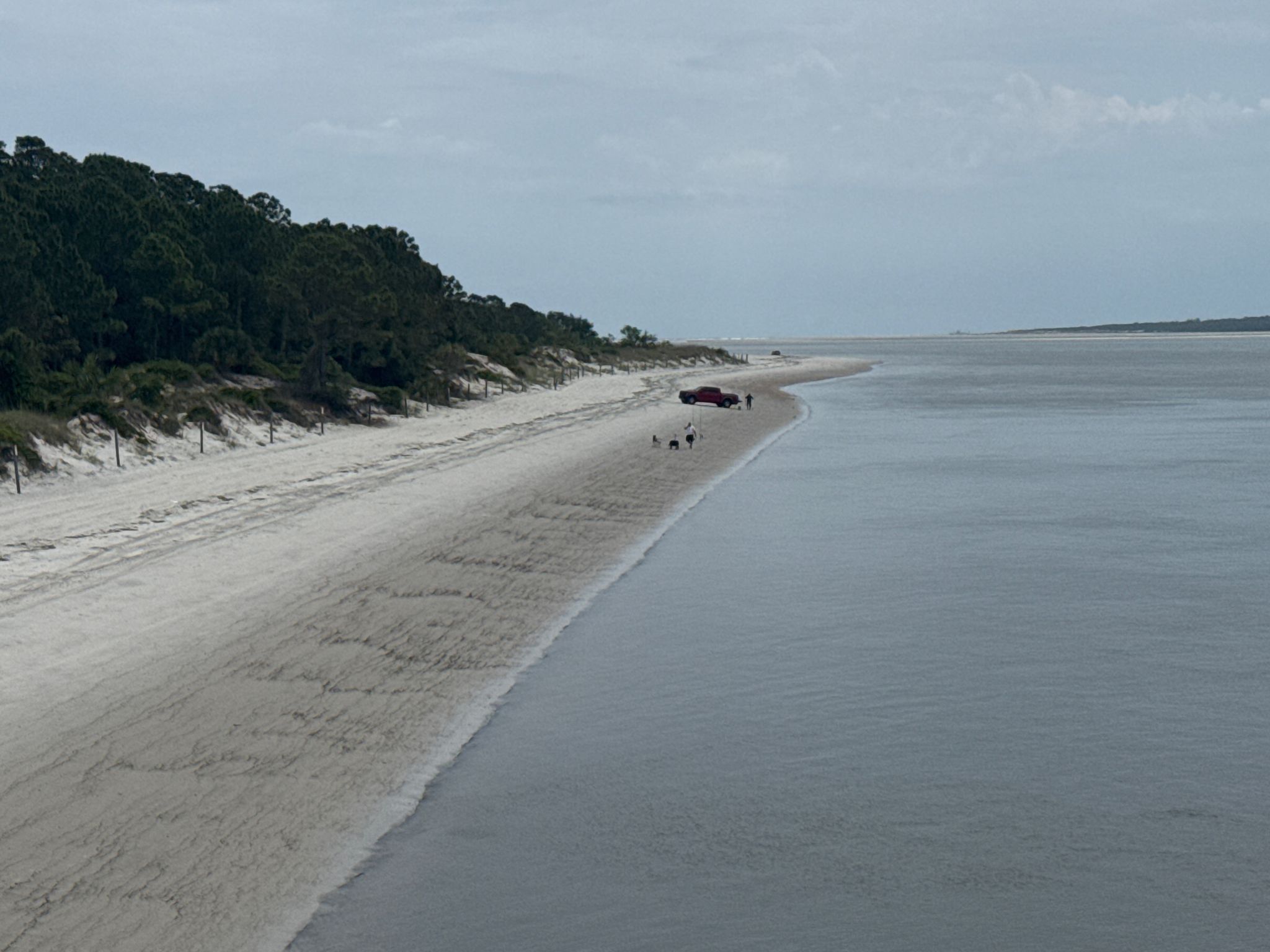 Overcast view of a wide sandy beach with people and a vehicle. - Big Talbot Island State Park – A1A Overlook loop from Timucuan Ecological & Historic Preserve